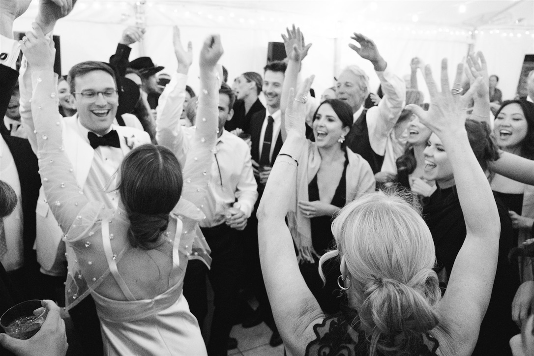 Group of people dancing and celebrating at a formal event, smiling and raising hands, in black and white.