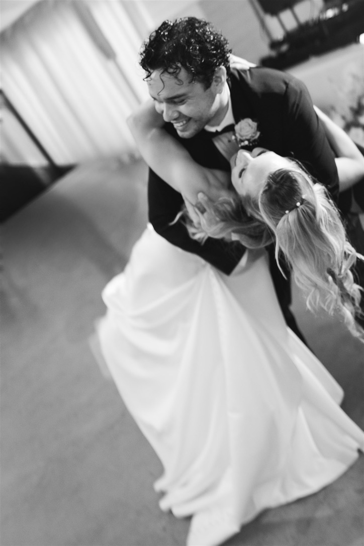 Couple dancing closely, smiling, woman in white dress, man in dark suit, indoor setting, joyful moment.
