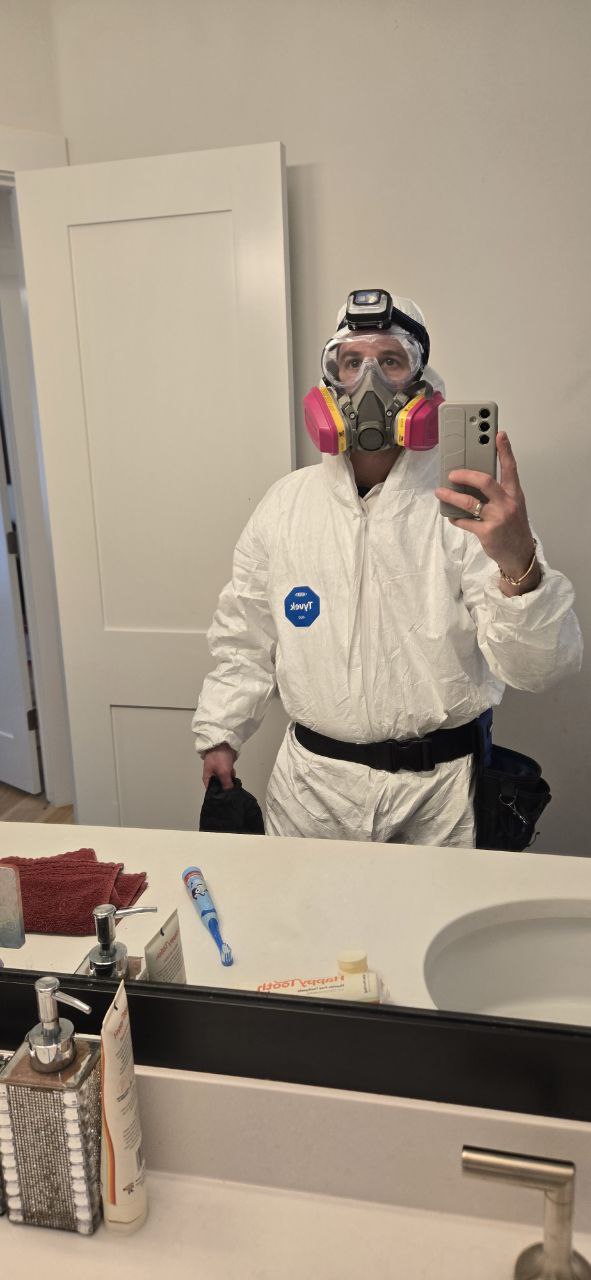 Person in protective suit, mask, and goggles taking a selfie in a bathroom mirror.