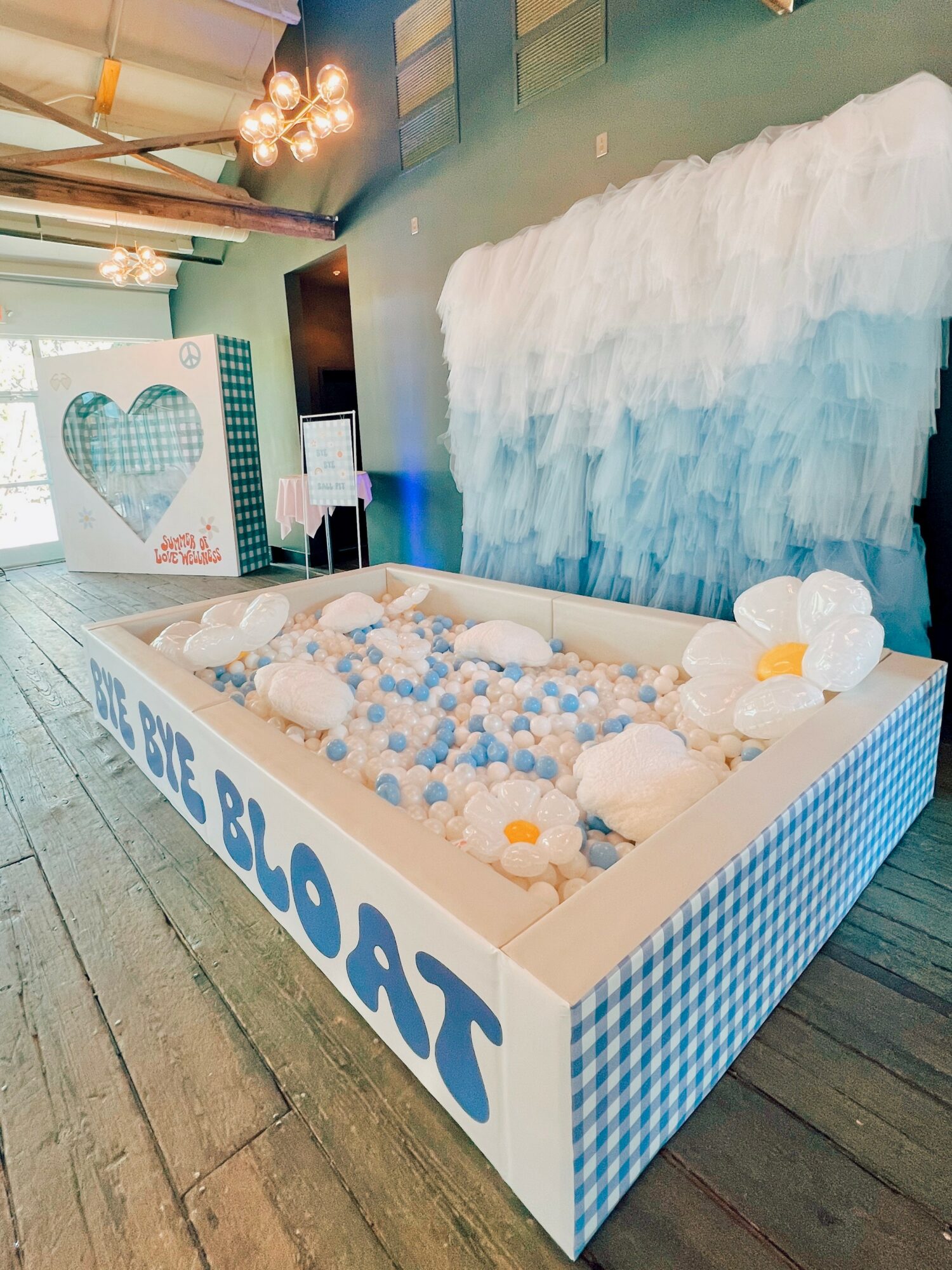 A decorated baby shower display with a blue and white theme, featuring a ball pit, cloud decoration, and heart-shaped backdrop.