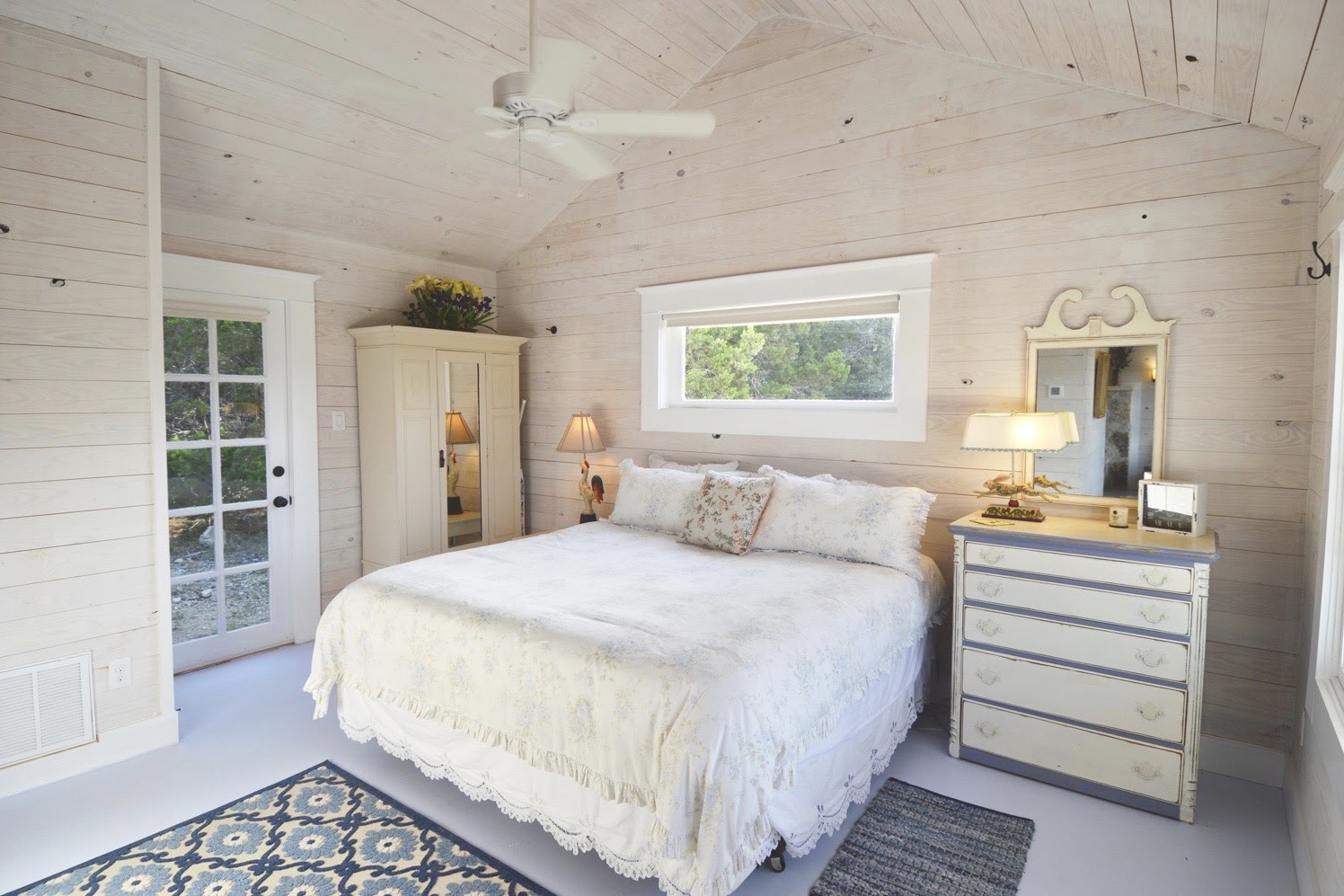 Bedroom with white walls, a bed with white bedding, a dresser with a mirror, and a window above the bed.