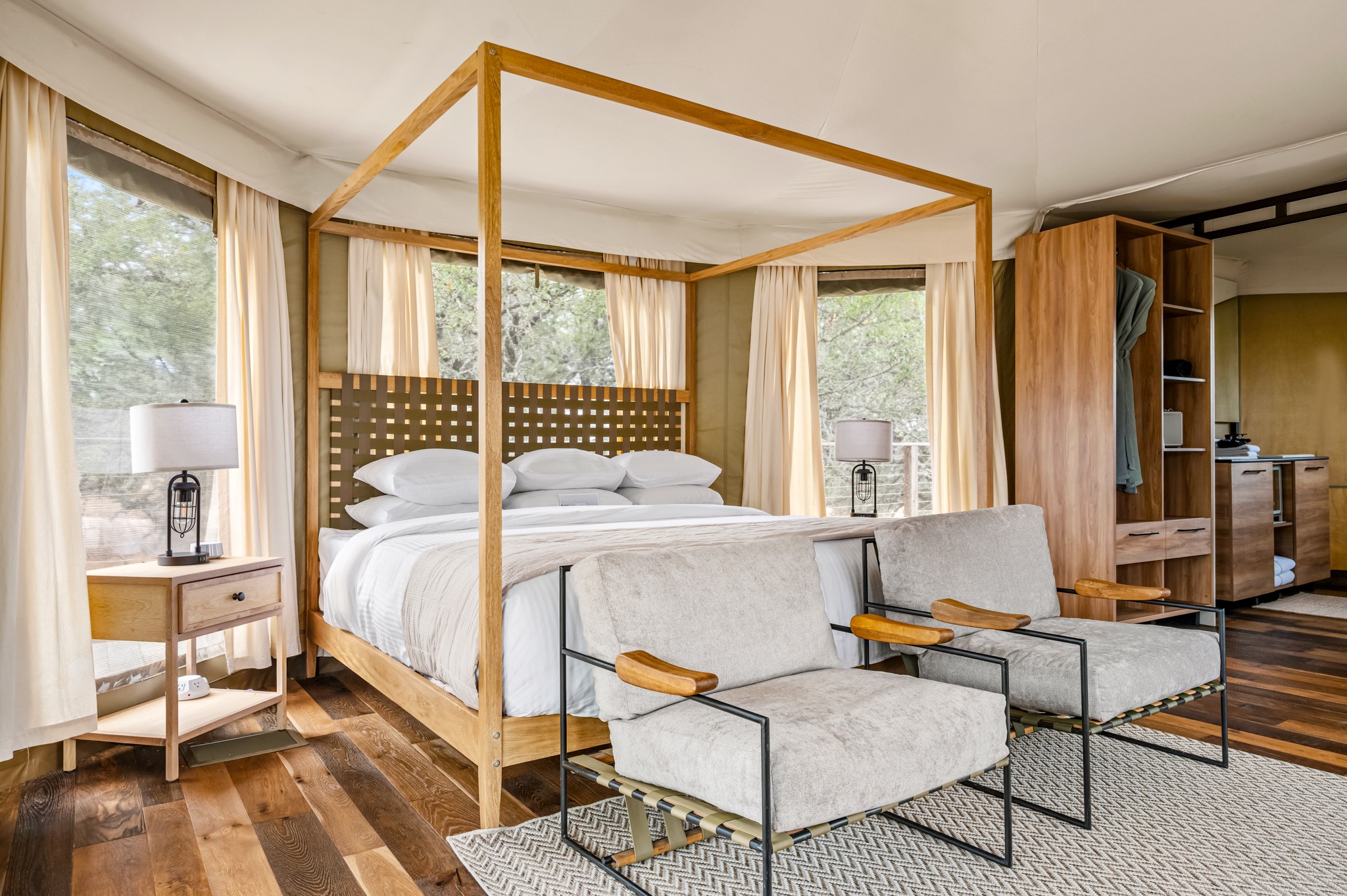 Bedroom with a four-poster bed, two chairs, side tables, and large windows with curtains.
