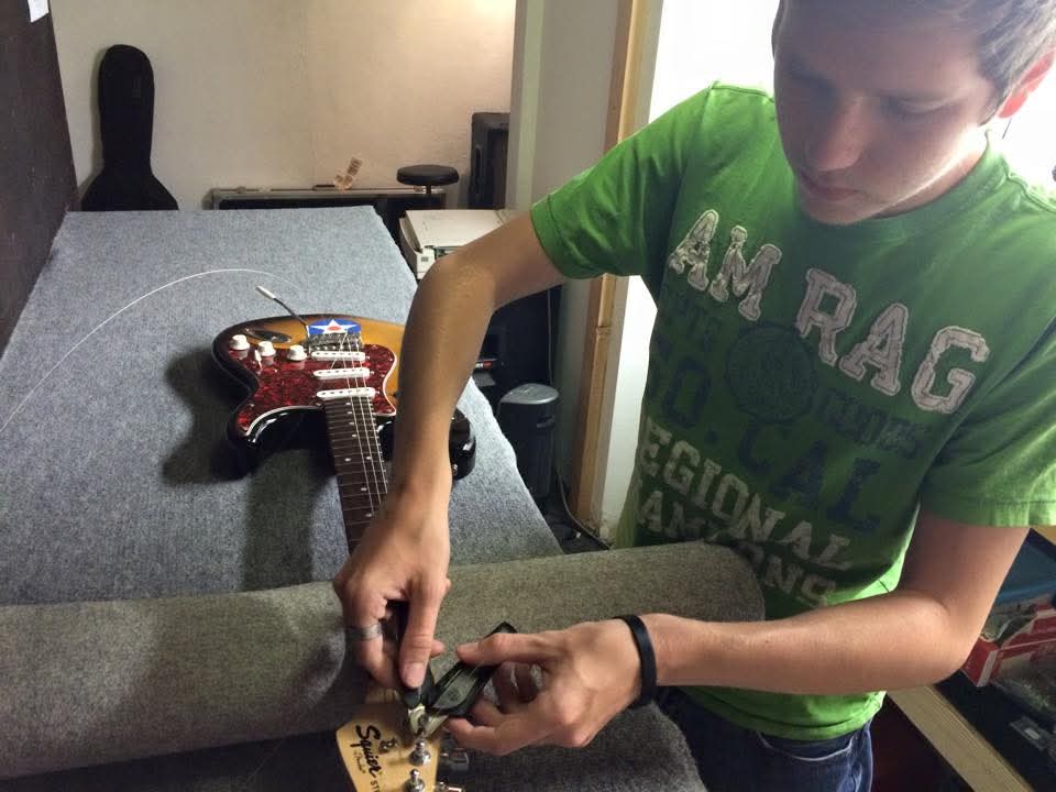 Child in green shirt using a tool on a gray fabric surface with a guitar-shaped object nearby.