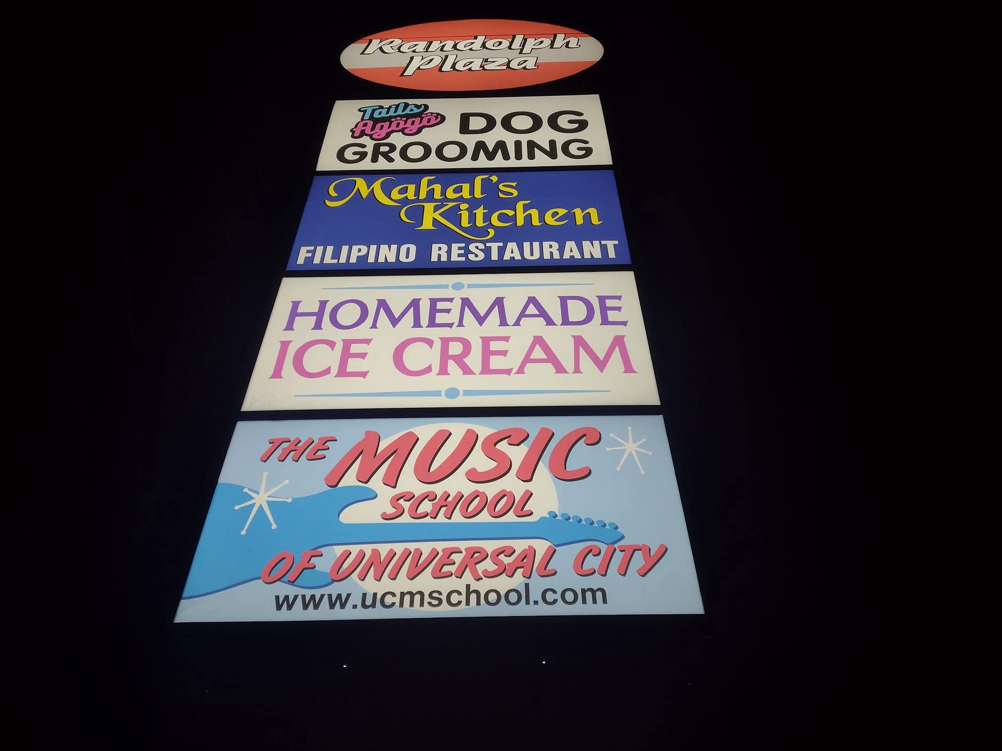 Vertical stack of six colorful signs advertising various businesses and services against a dark background.