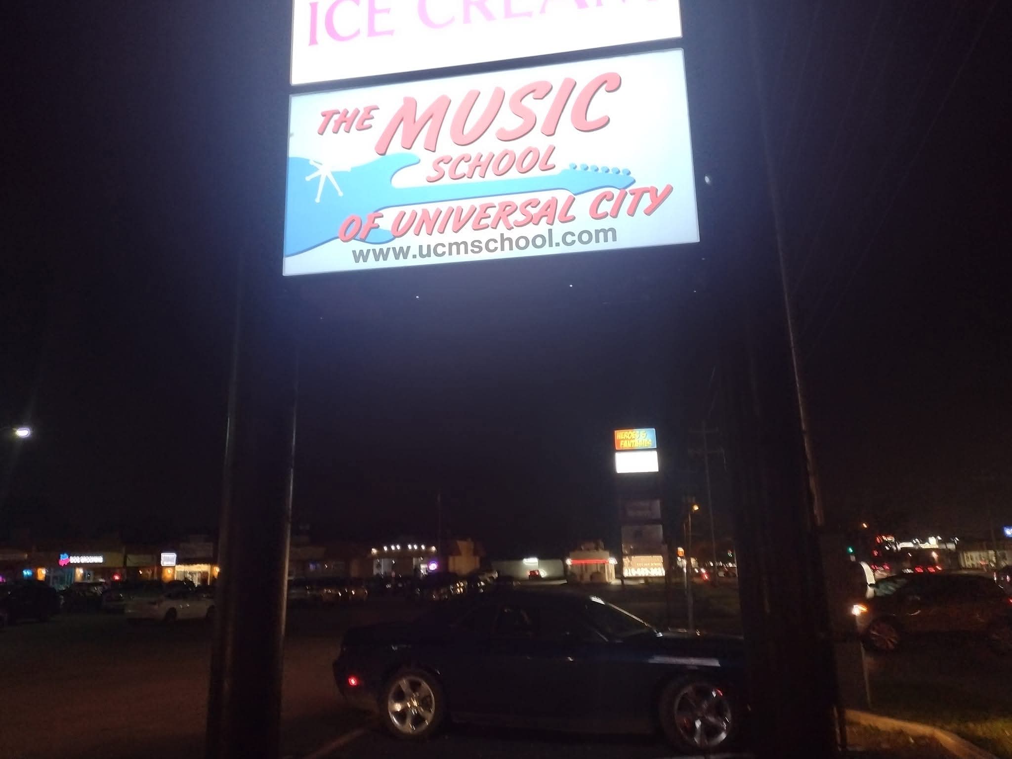 Nighttime billboard advertising music school, with cars and city lights in the background.