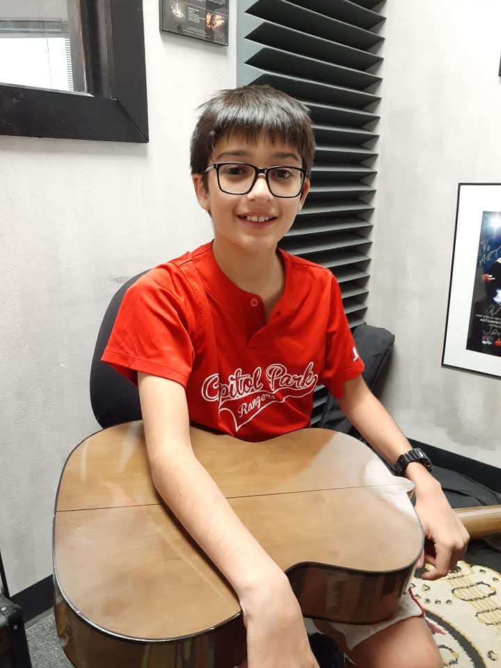 Child with glasses and short hair sitting at a table, smiling, wearing a red T-shirt, in a room with black and white decor.