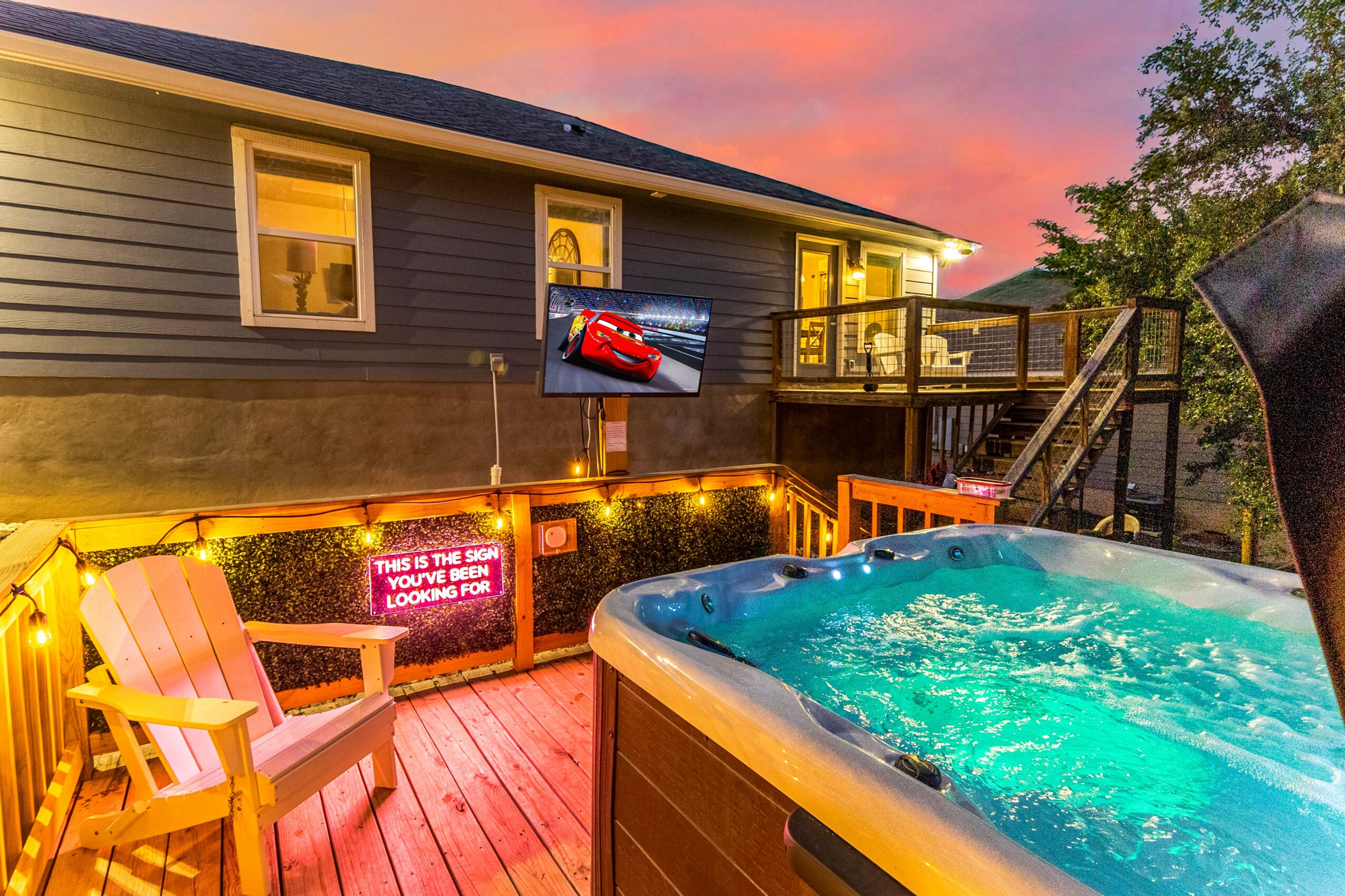 Backyard with hot tub, wooden deck, outdoor seating, and a house with windows at sunset sky.
