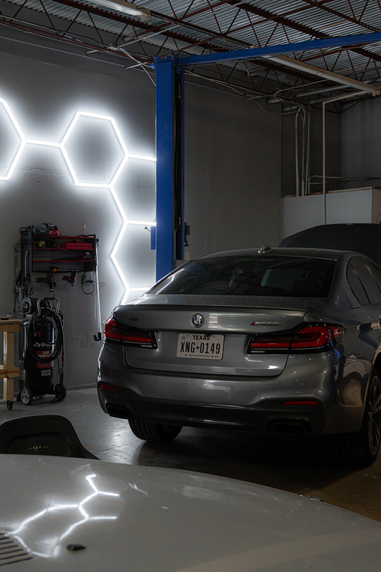 Silver car parked inside a garage with illuminated hexagonal wall design and industrial ceiling.