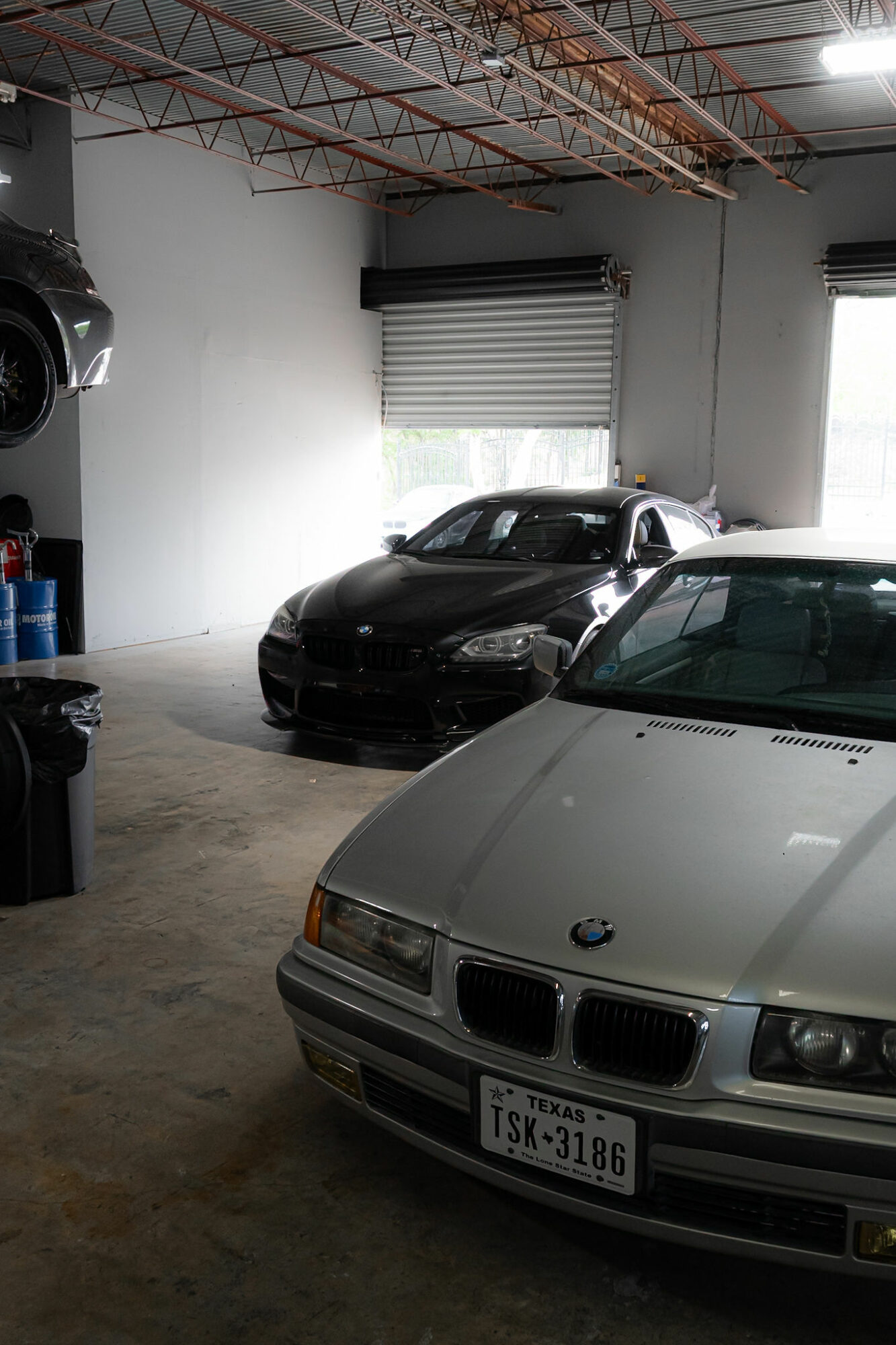 Indoor garage with two parked cars, one black and one silver, and windows with blinds.