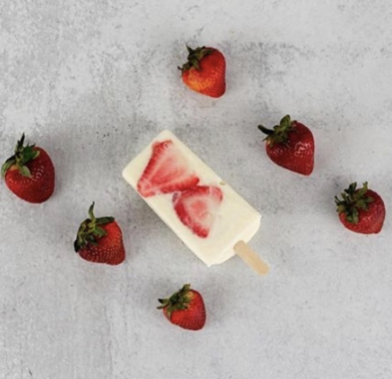 Strawberry-flavored ice cream bar surrounded by six strawberries on a light surface.