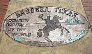 Oval concrete sign with text and a cowboy riding a bucking horse, located on a brick sidewalk.