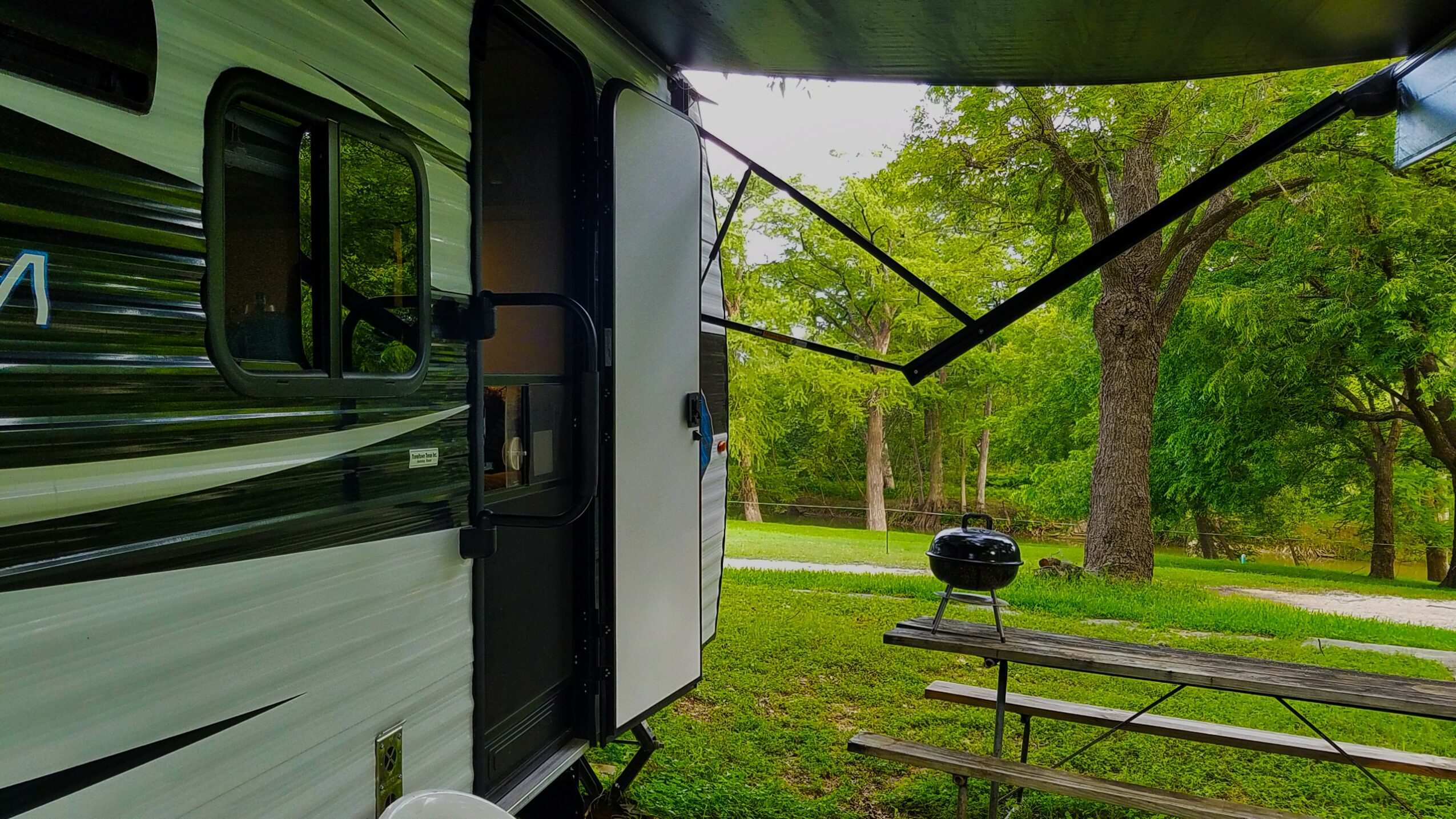 RV door open with a picnic table and trees in a park setting.