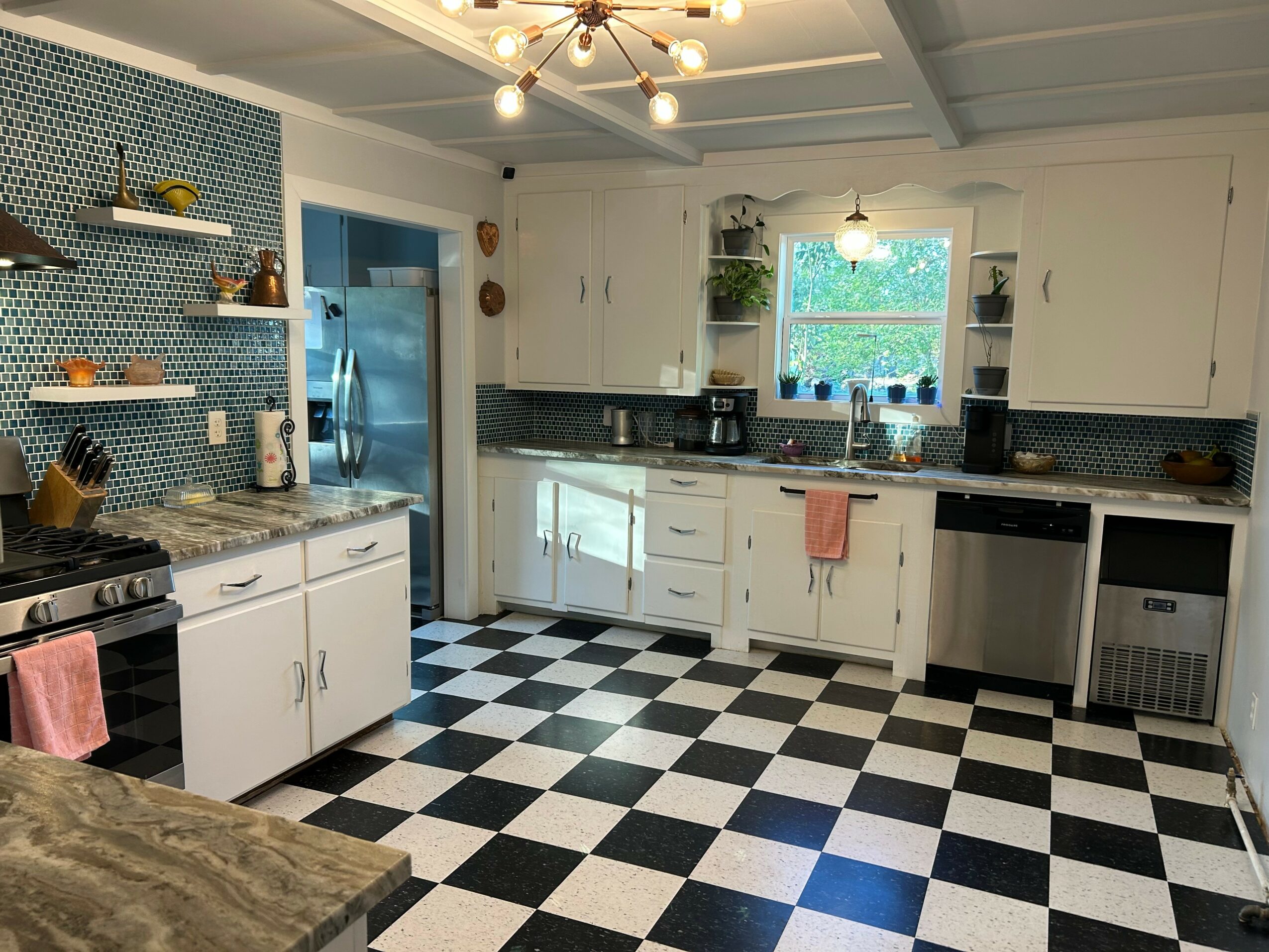 Kitchen with white cabinets, black and white checkered floor, window, and appliances including refrigerator and stove.