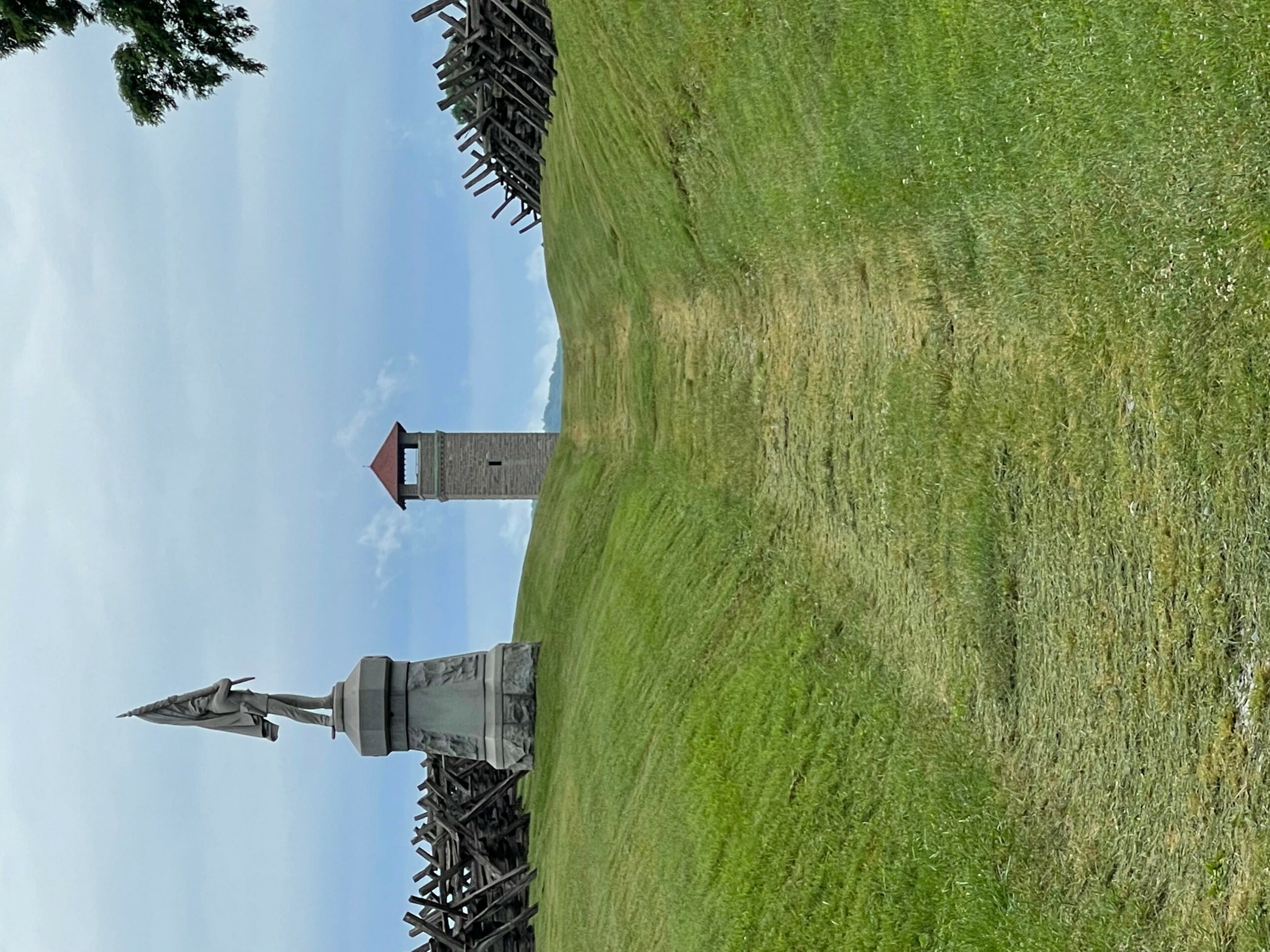 A grassy field with a monument and a tower in the background under a cloudy sky.
