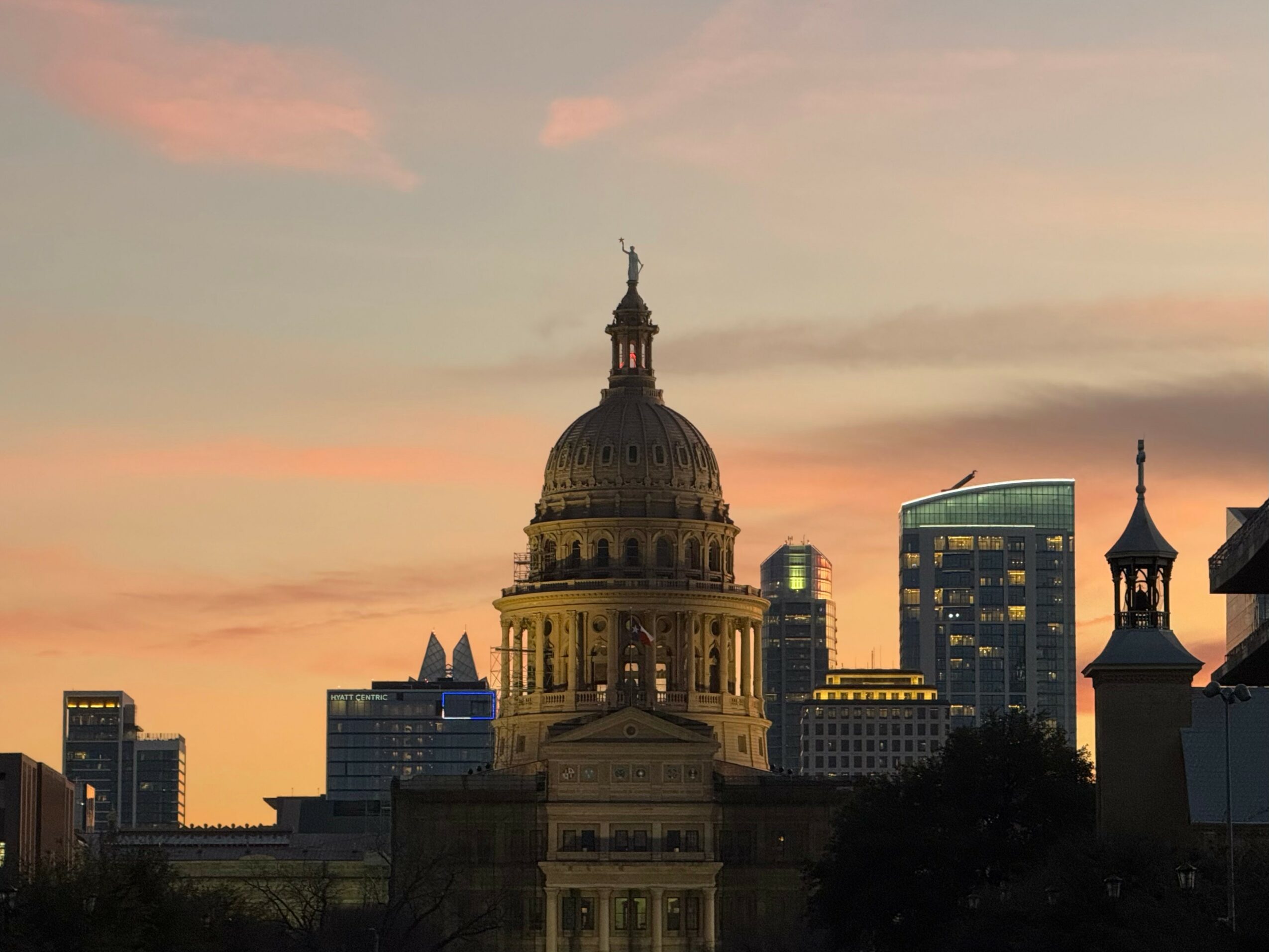 City skyline at sunset with a prominent domed building and modern skyscrapers in the background.