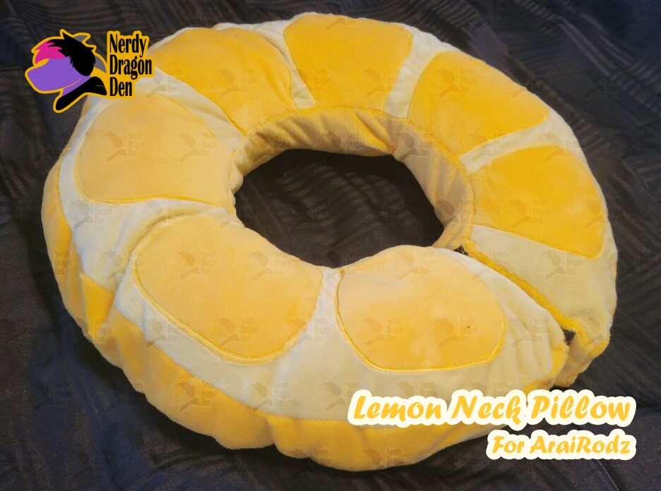 Yellow lemon-shaped neck pillow with white accents, circular design, on a dark surface.
