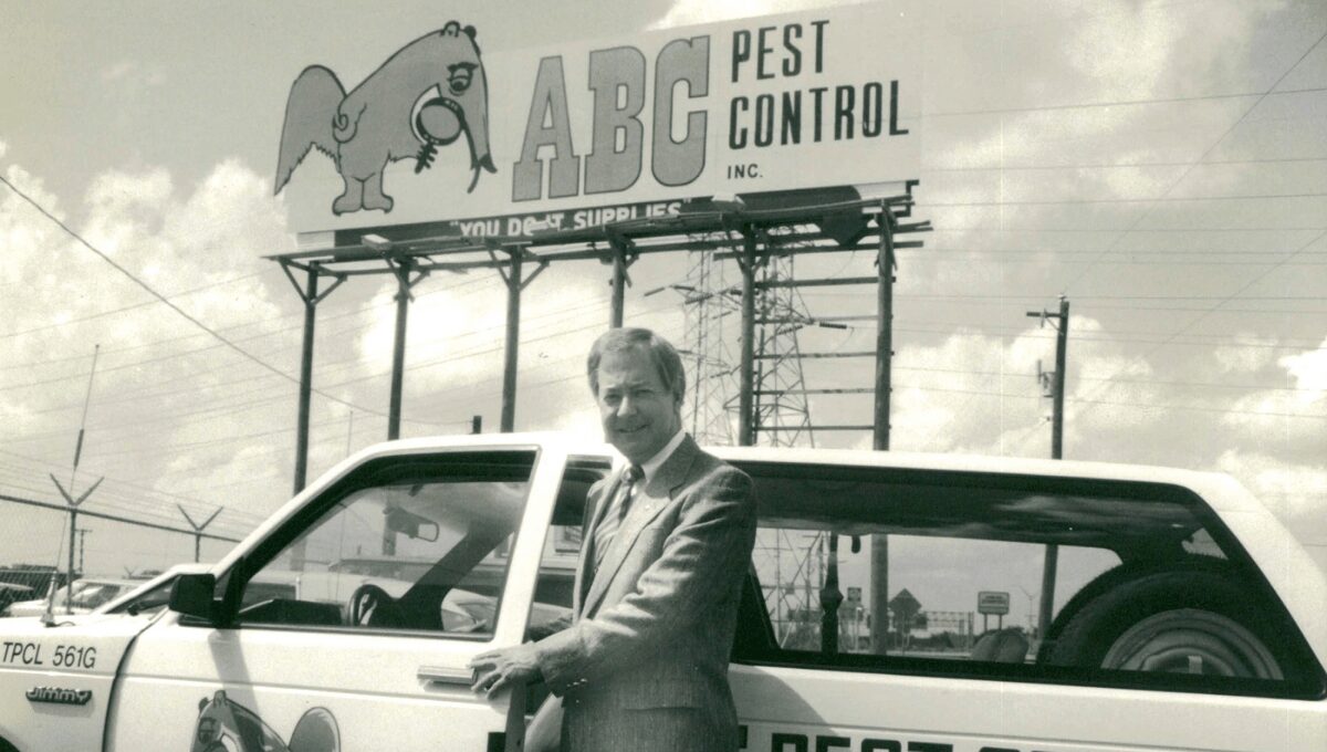 Man in suit standing next to a white truck with a sign for ABC Pest Control in the background.