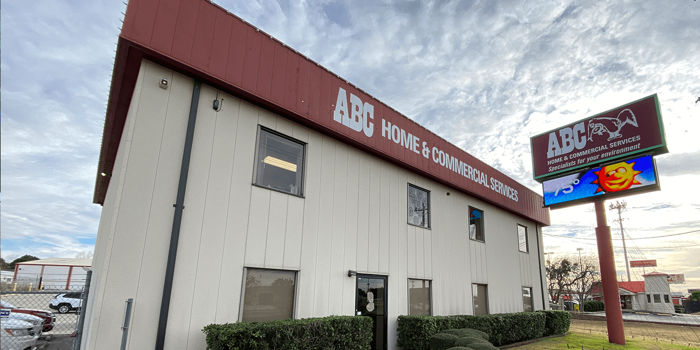 Two-story building with a red roof and white walls, displaying signs for ABC Home & Commercial Services and a digital billboard.