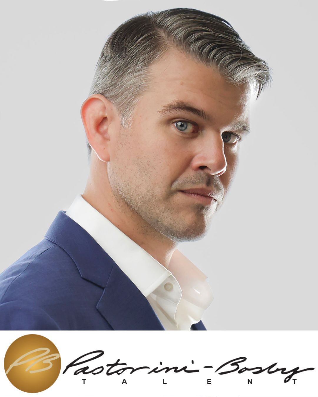 Portrait of a man with gray hair, blue eyes, wearing a navy suit and white shirt, looking sideways.