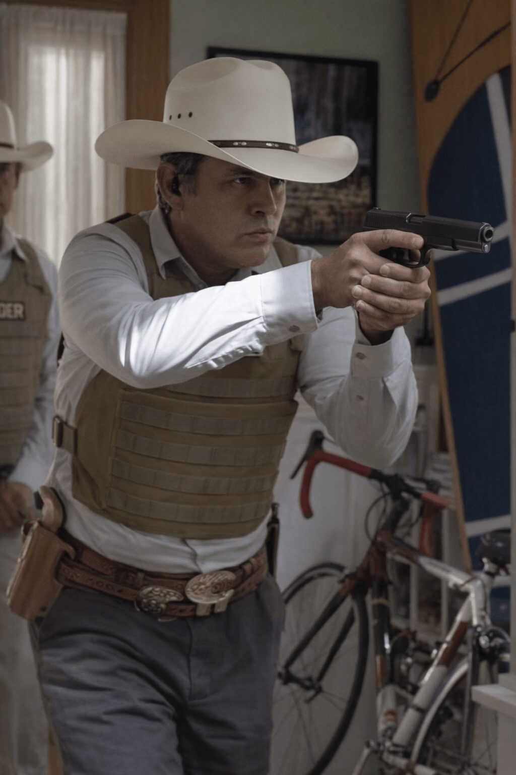 Person in cowboy hat aiming a gun indoors, with a bicycle nearby and a person in the background.