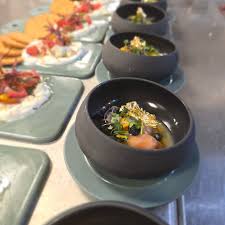 Black bowl with food, placed on a gray plate, on a table with other dishes in the background.