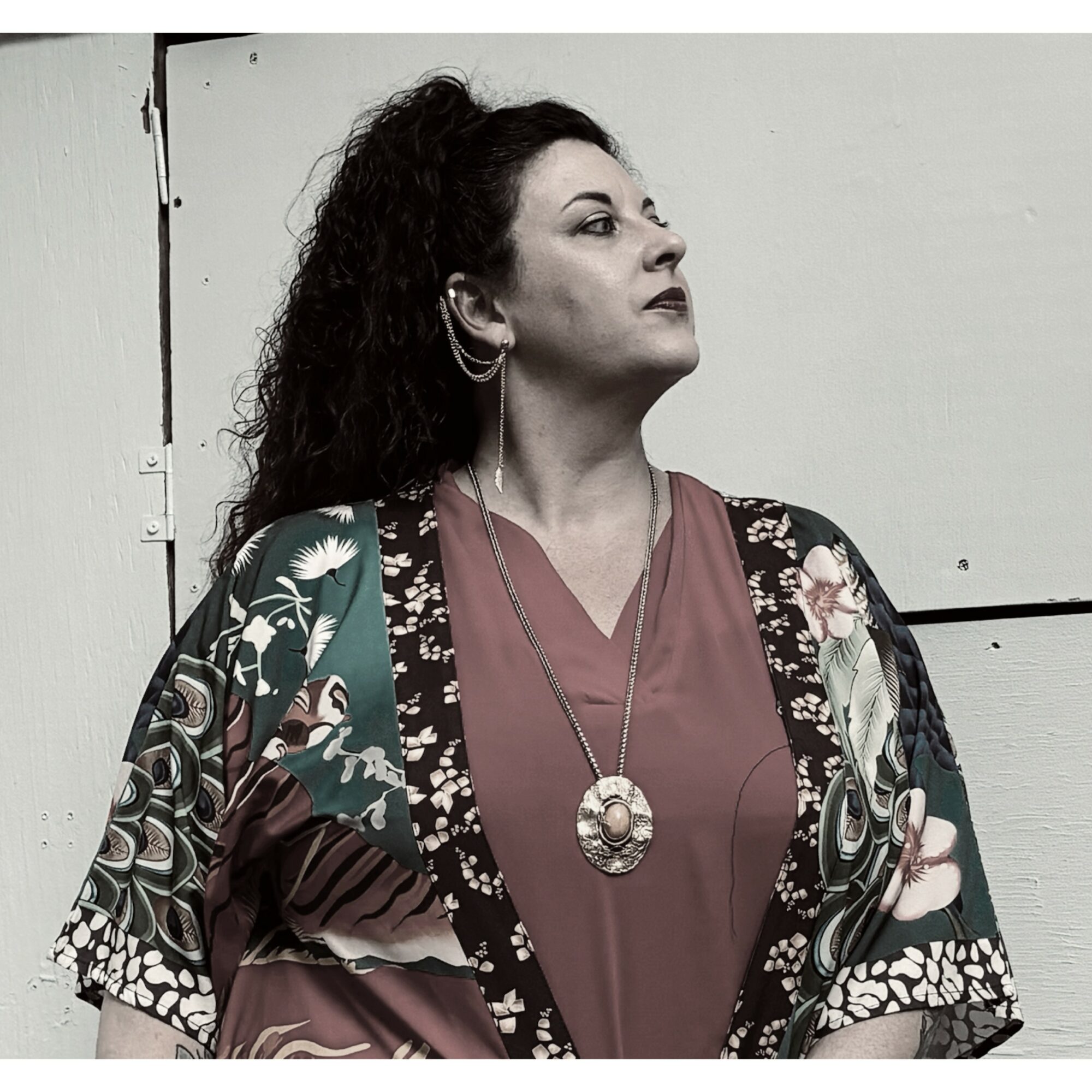 Woman with curly hair wearing a floral kimono and a necklace, looking to the side against a plain background.