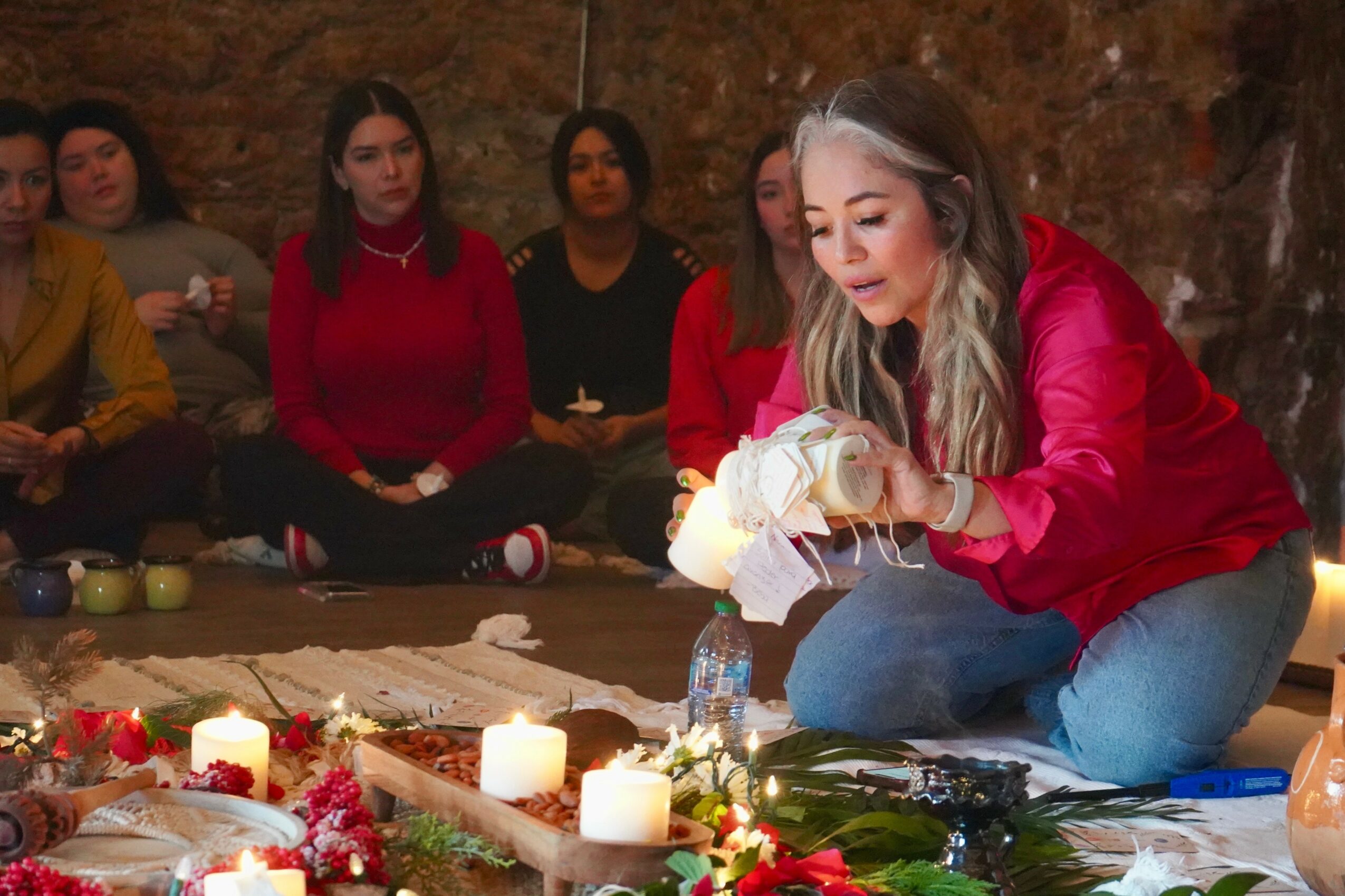 Woman in red jacket lighting candles on a table with others watching, in a dimly lit setting.
