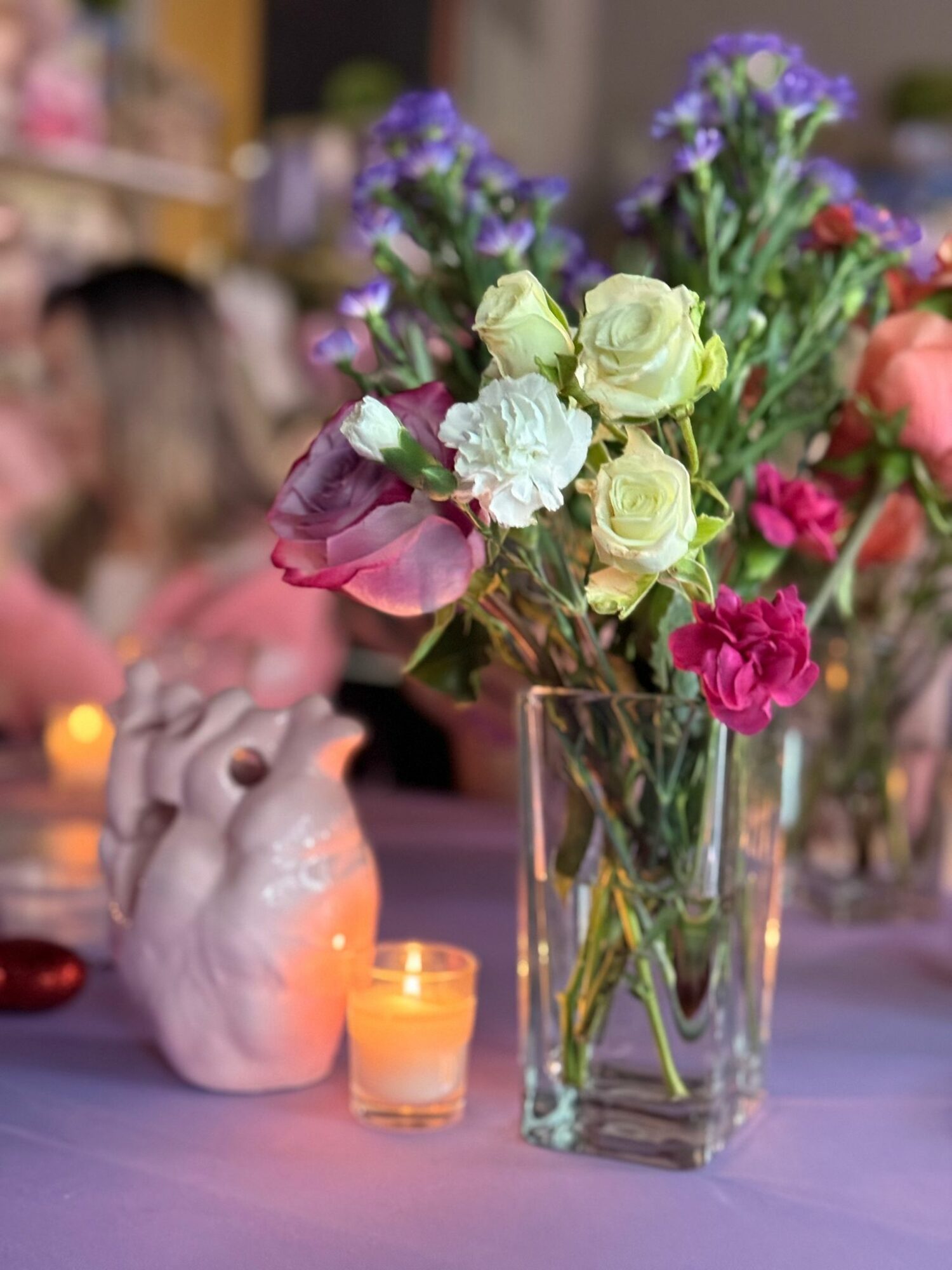 Vase with mixed flowers including roses and carnations, candles, and a ceramic rabbit figurine on a table.