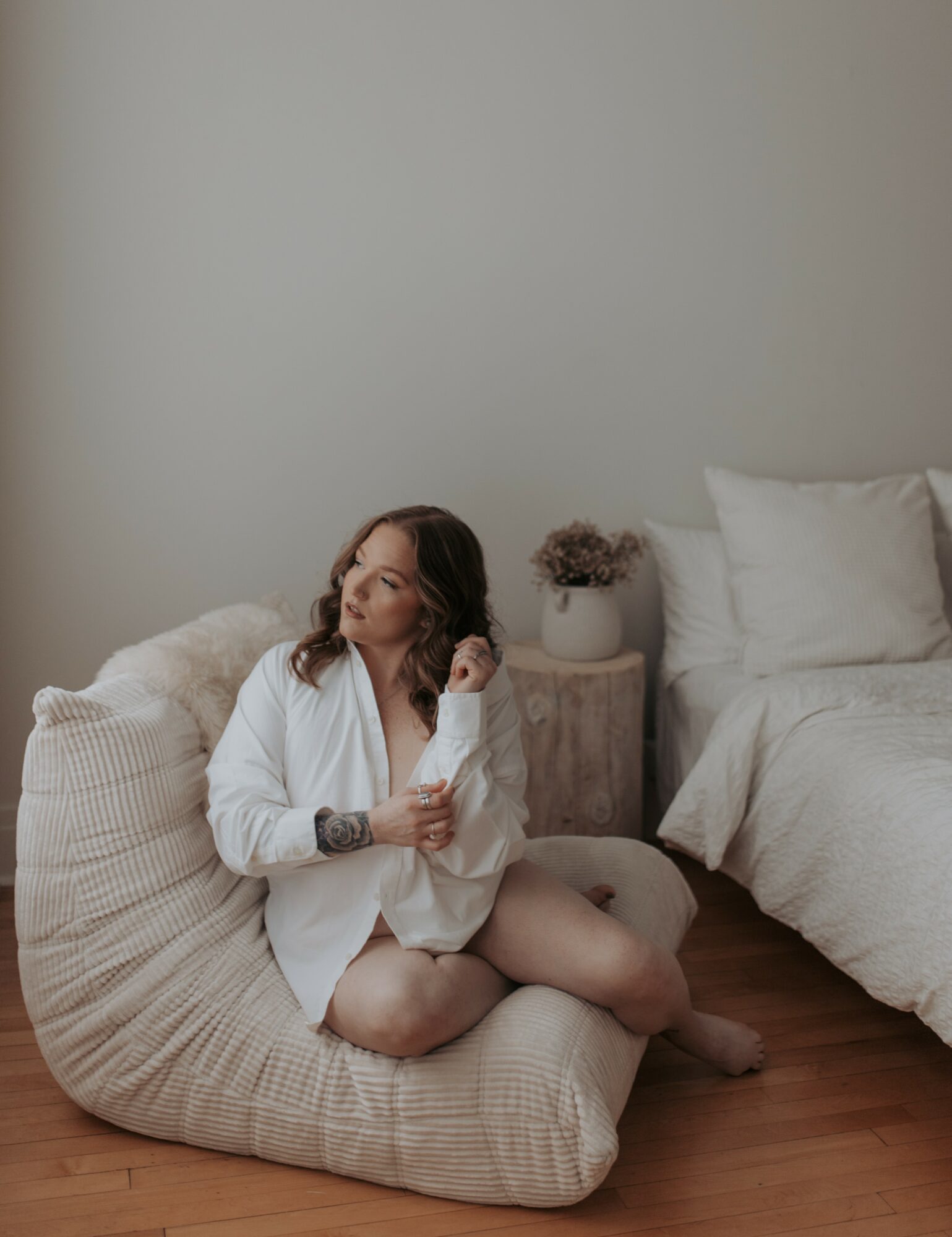 Woman sitting on a bean bag chair in a bedroom, with a bed and nightstand in the background.