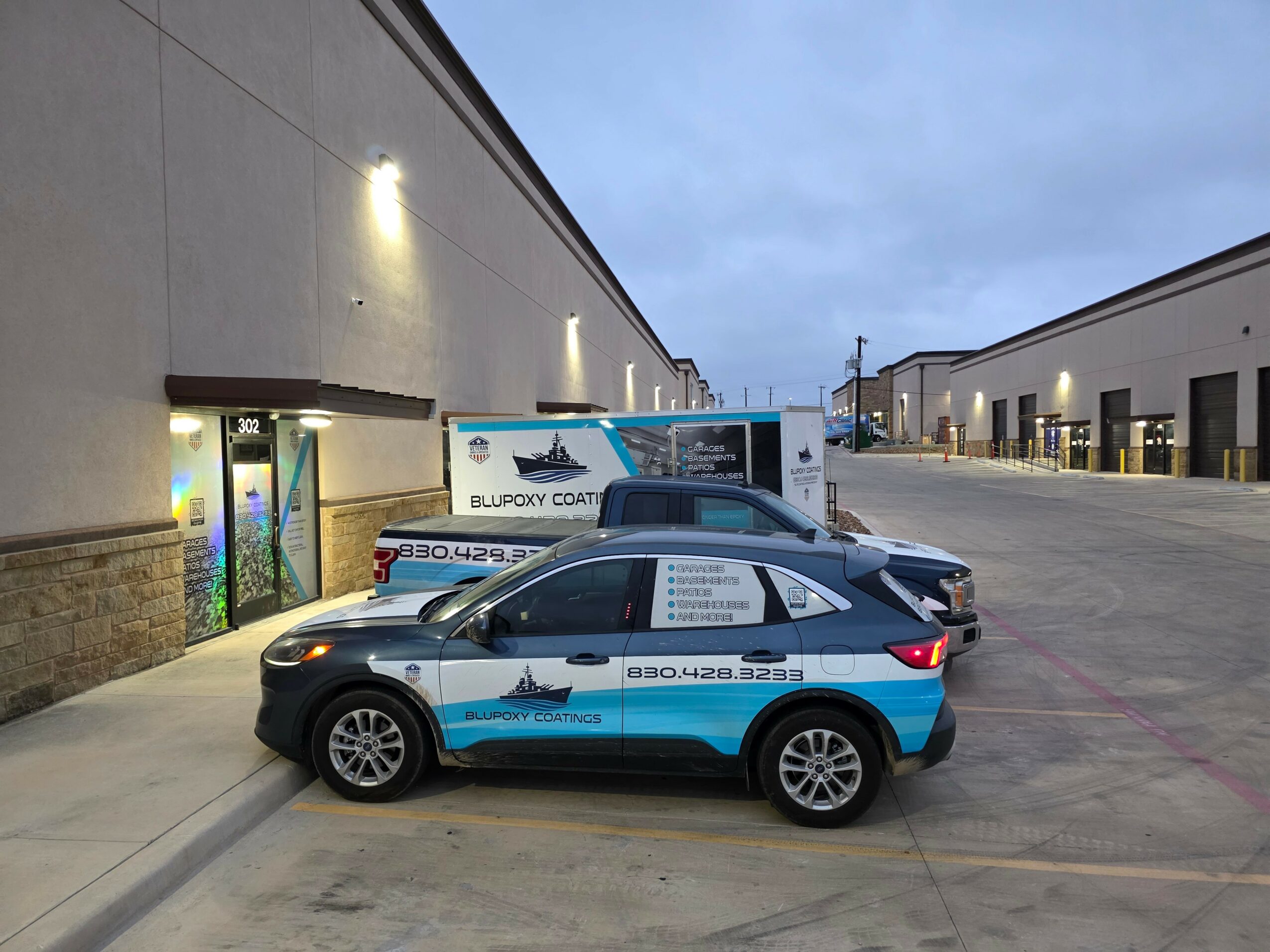 Parking lot with two blue and white vehicles parked near a building, cloudy sky in background.