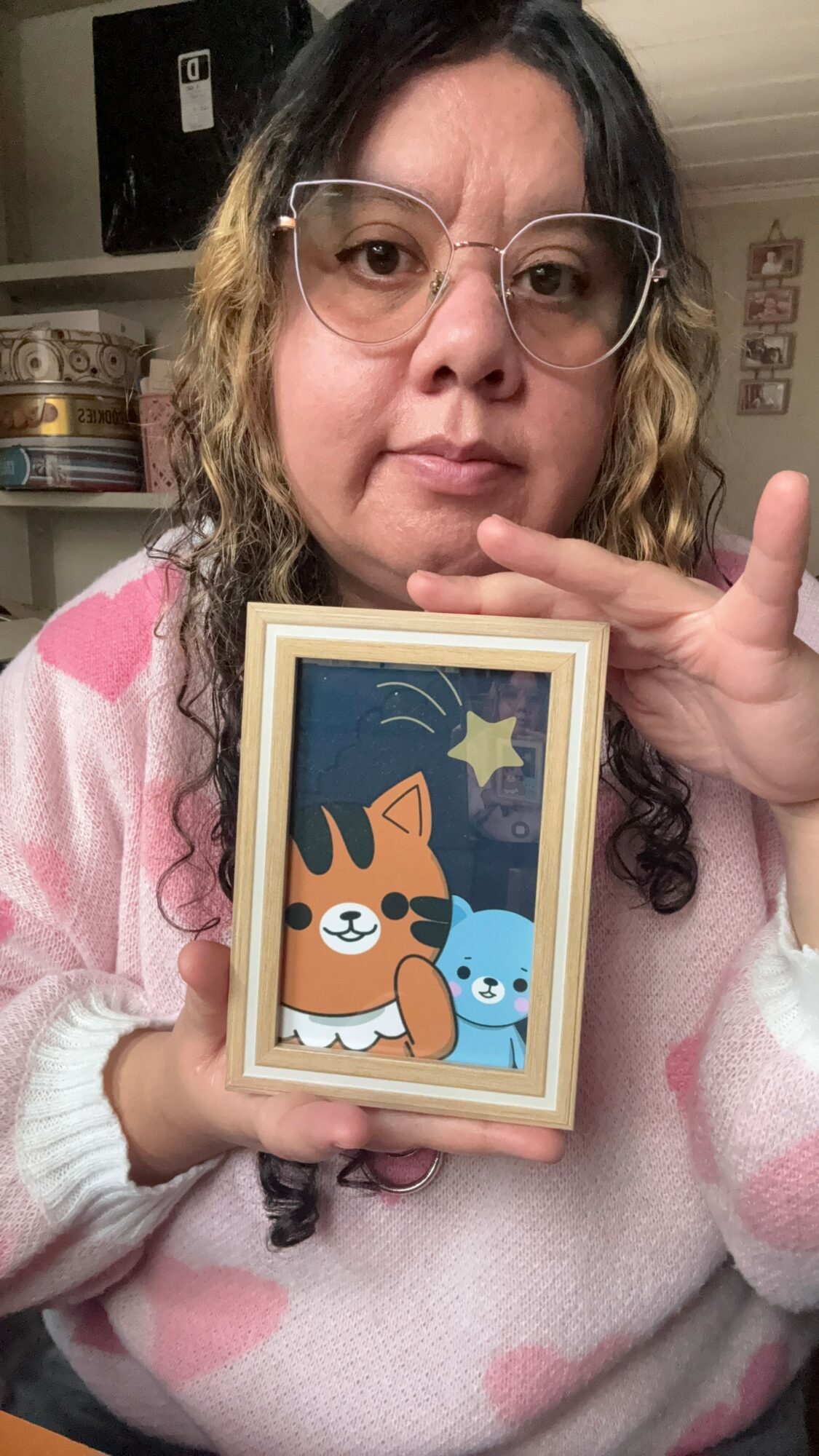 Person with glasses holding a framed illustration of a dog and a blue creature under a starry sky.