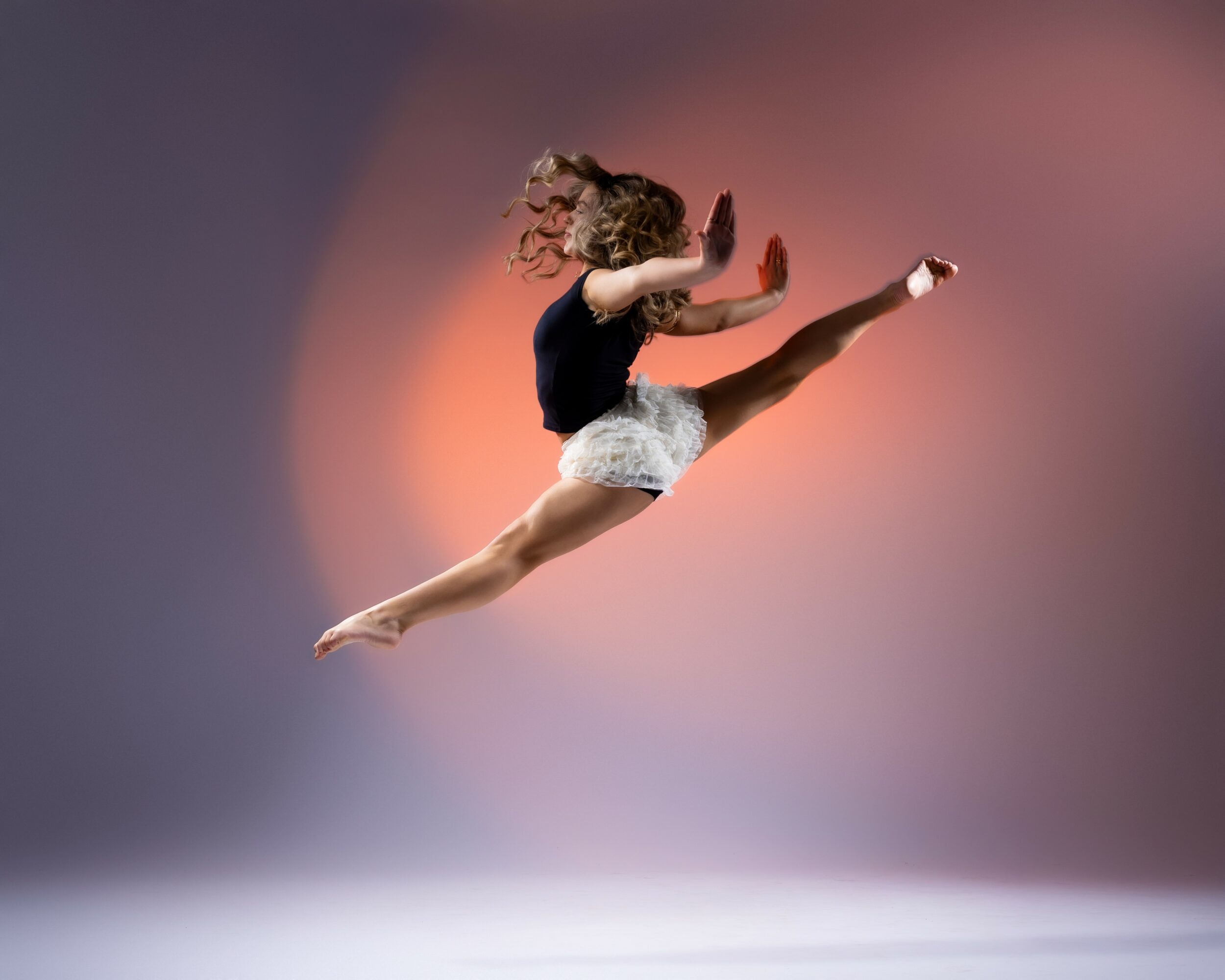 A female gymnast in mid-air performing a split leap with arms and legs extended, against a gradient background.