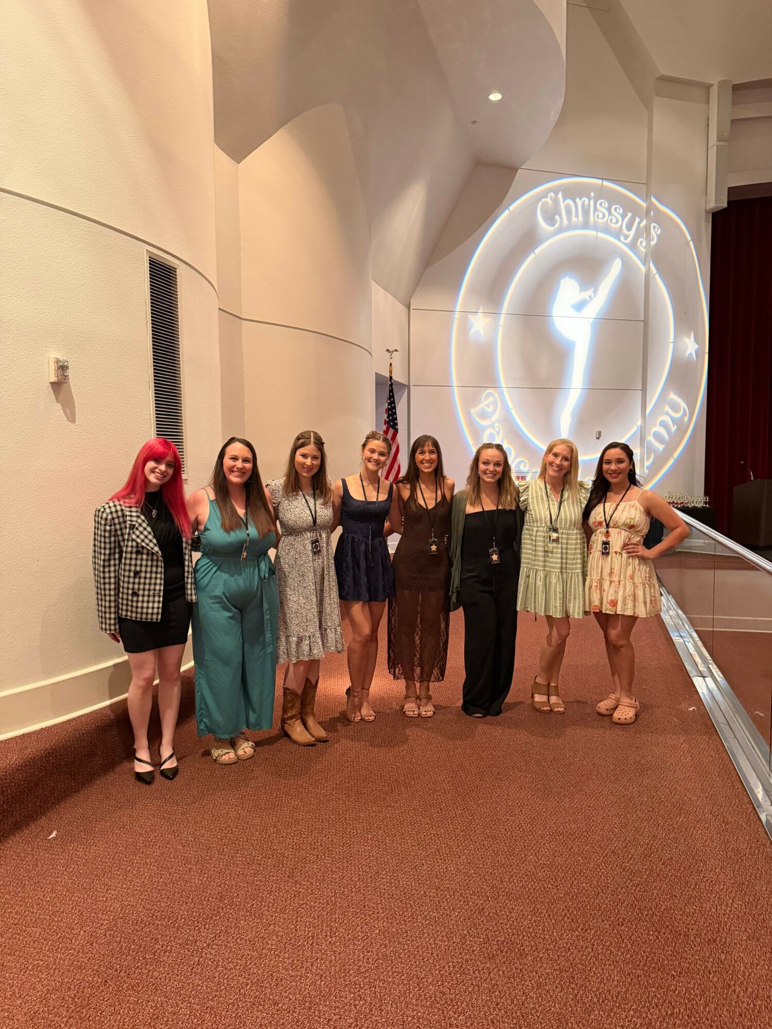 Group of seven women standing in a hallway with a circular logo projected on the wall behind them.