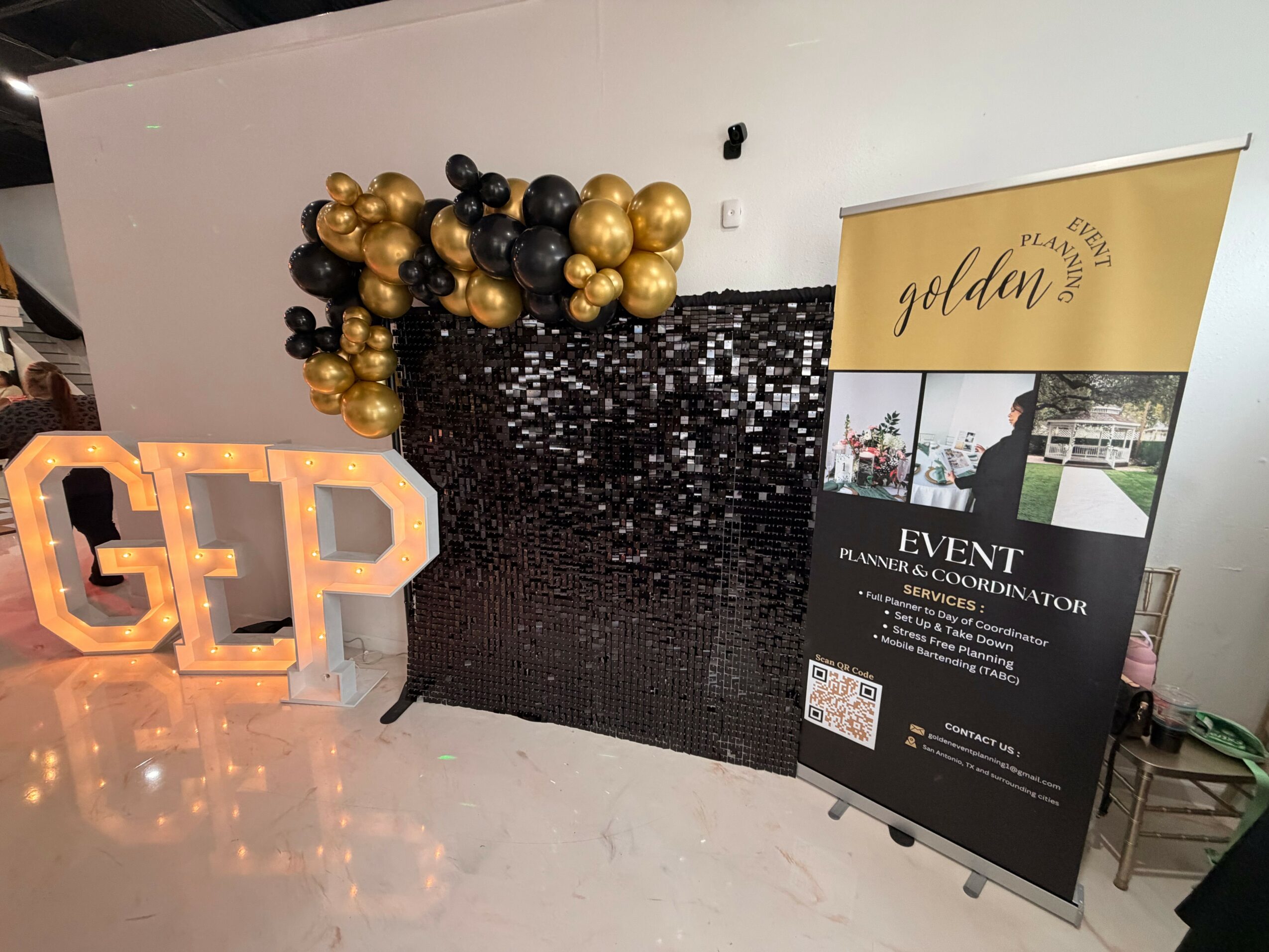 Decorative backdrop with black sequins, gold and black balloons, illuminated 'GEP' sign, and event banner for Golden event.