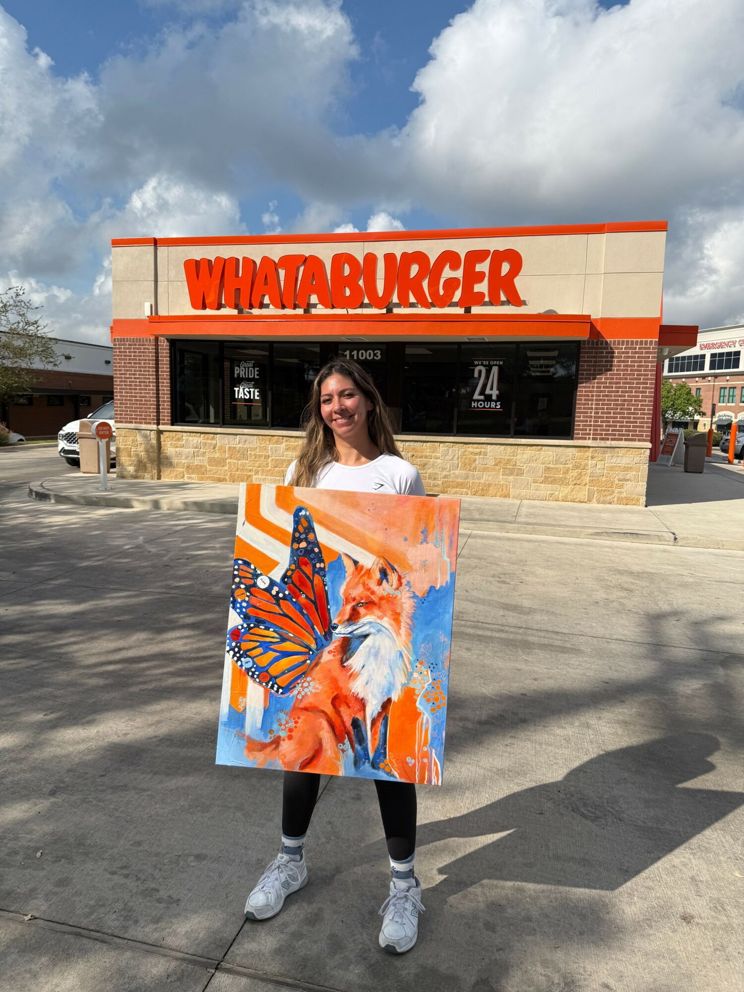 Person holding a colorful painting of a fox with butterfly wings outside a Whataburger restaurant.