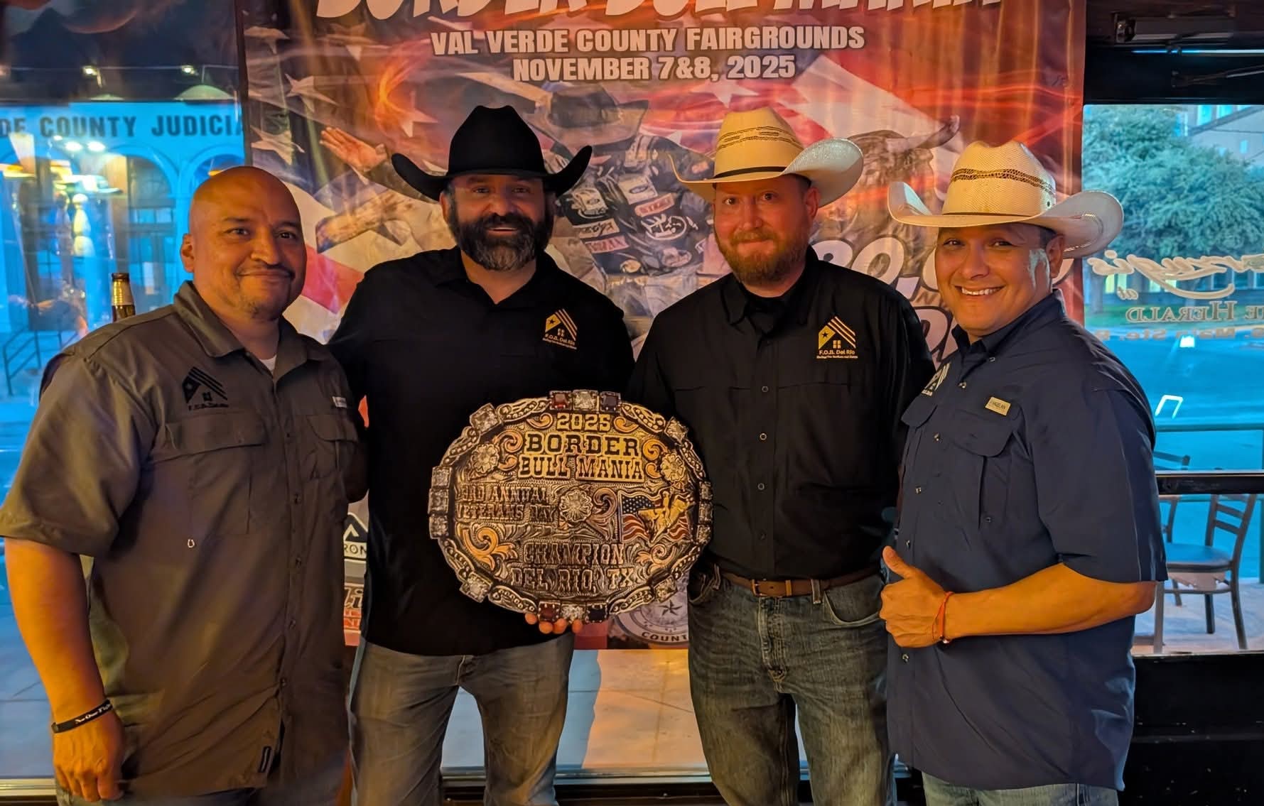 Four people standing indoors, holding a large decorative plaque, with a colorful banner in the background.
