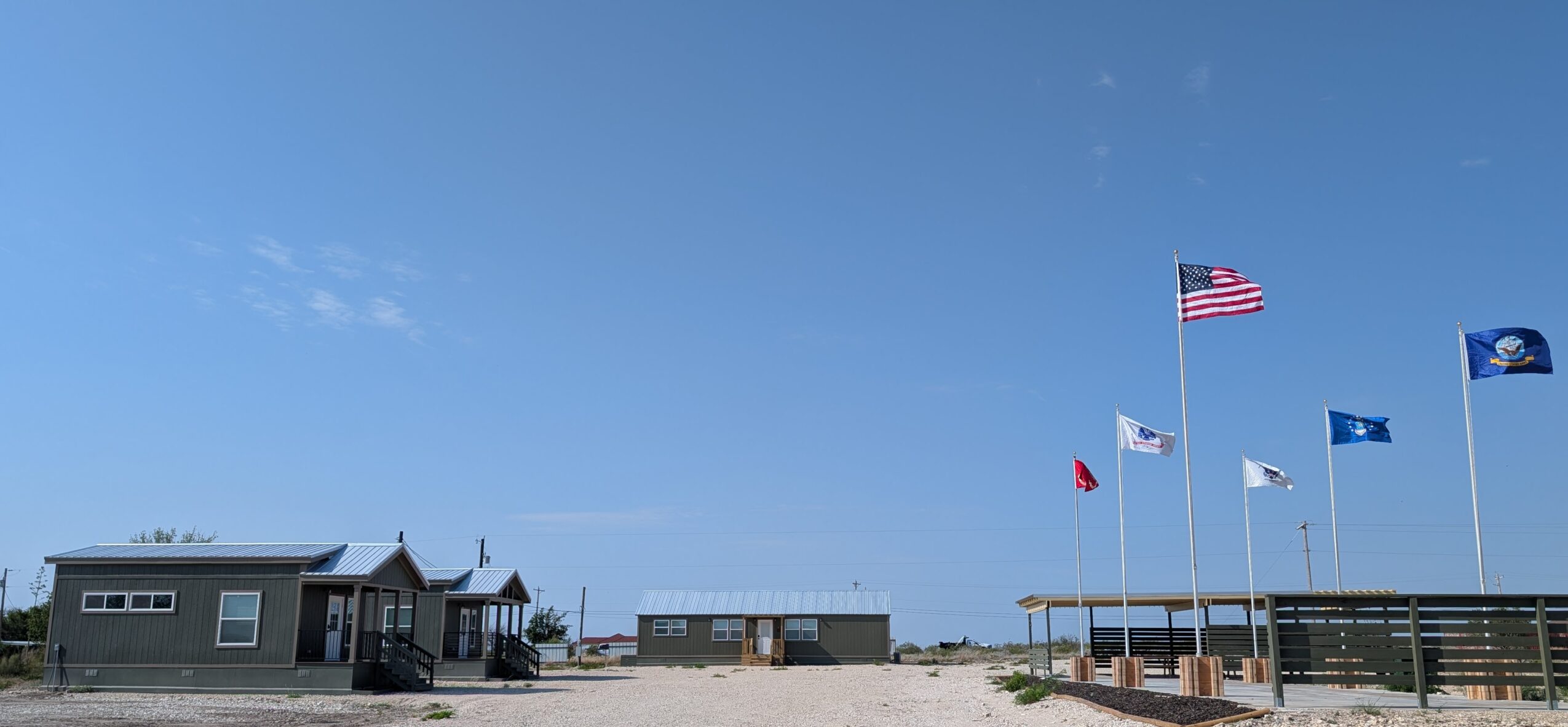 Beach scene with flags, small building, and clear blue sky, no people visible, sandy ground, and a wooden walkway.