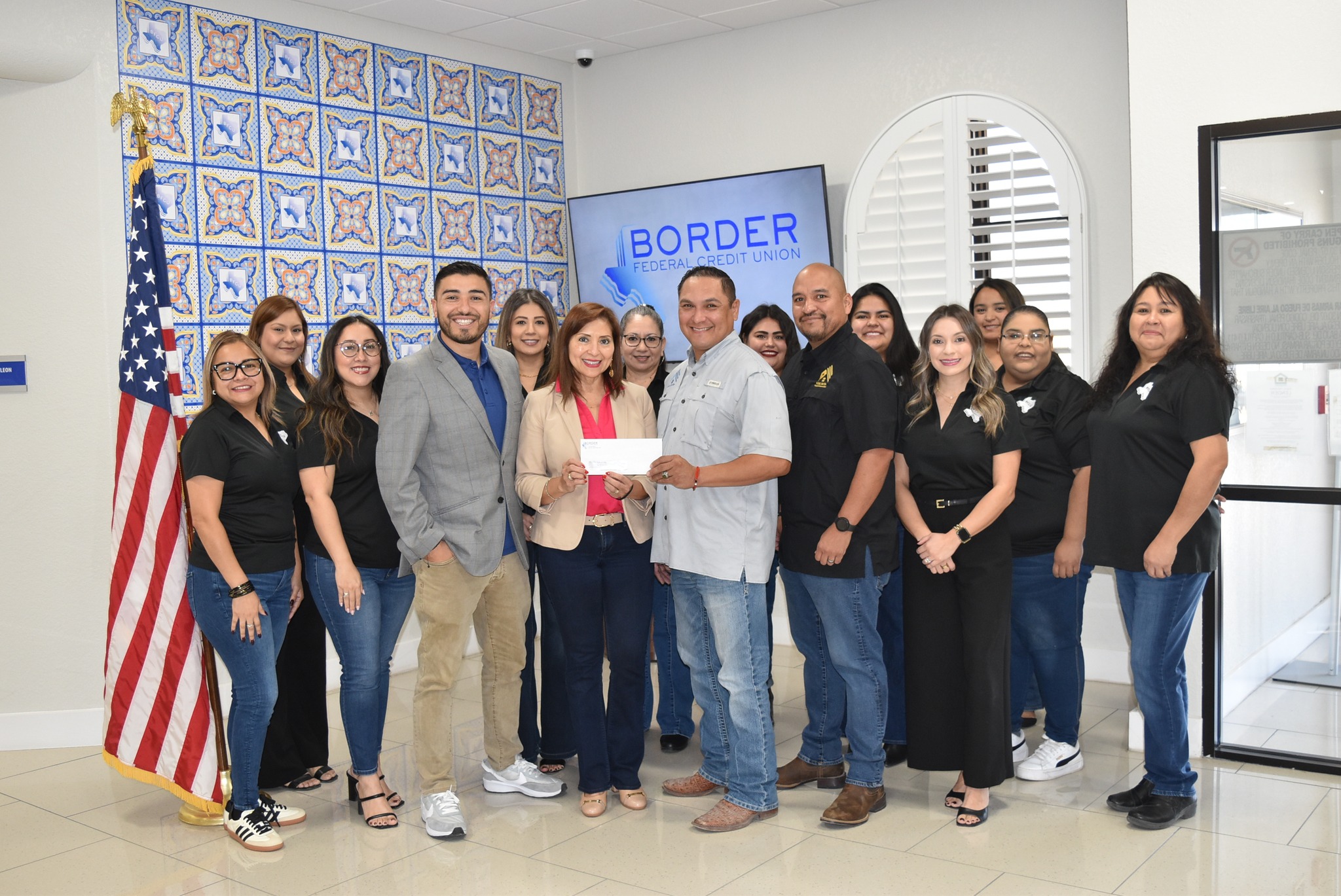 Group of people standing indoors, some holding a document, with a sign that says 'BORDER' behind them.