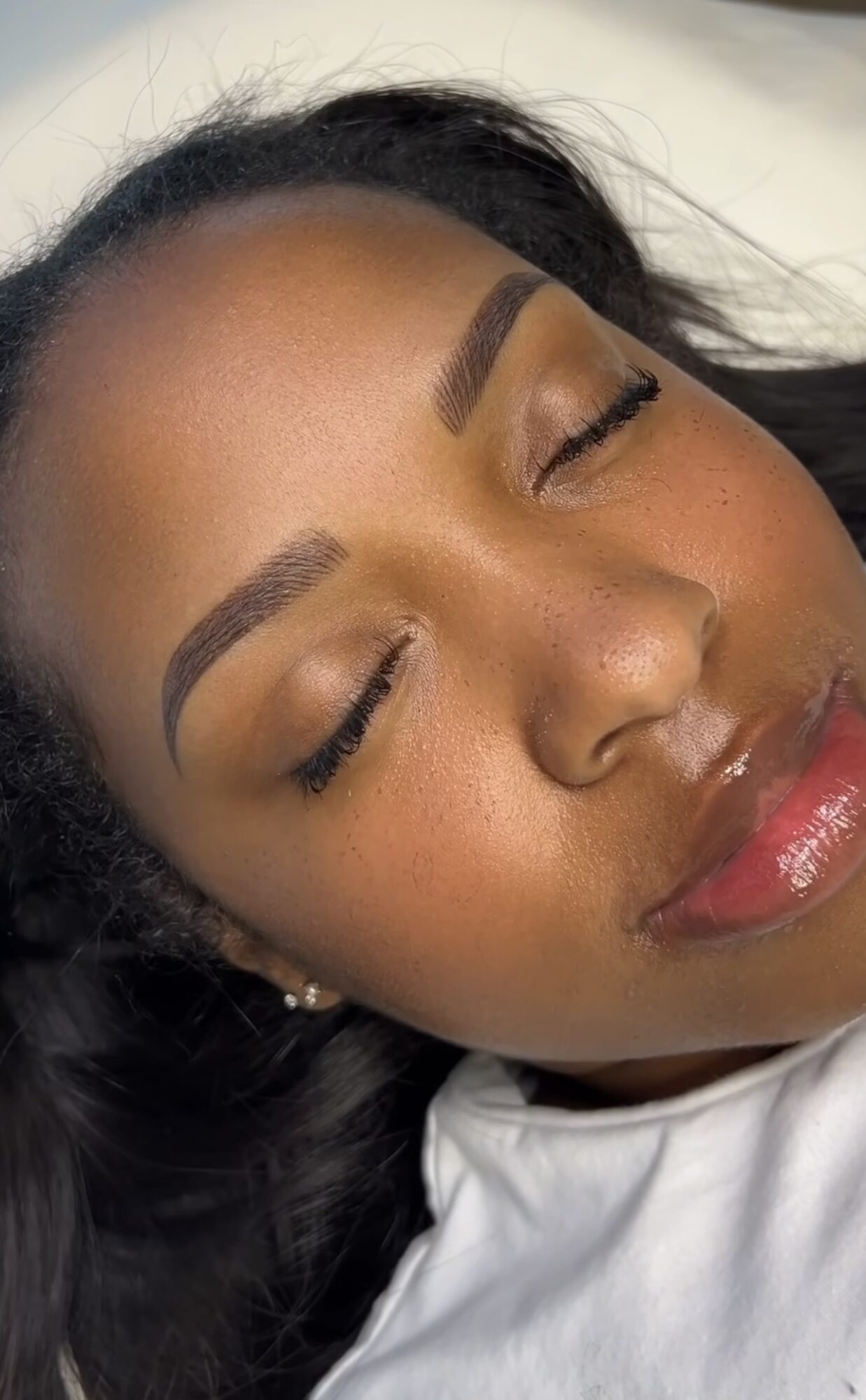 Close-up of a woman's face with closed eyes, makeup, and glossy lips, lying down with hair spread around.