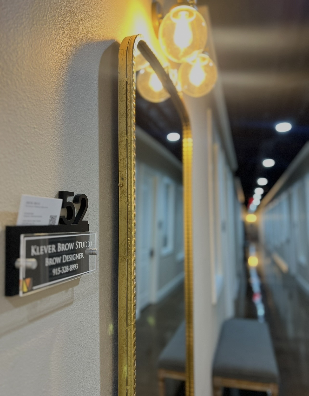 Hallway with illuminated signs and a mirror on the wall, with a bench along the corridor, blurred background.