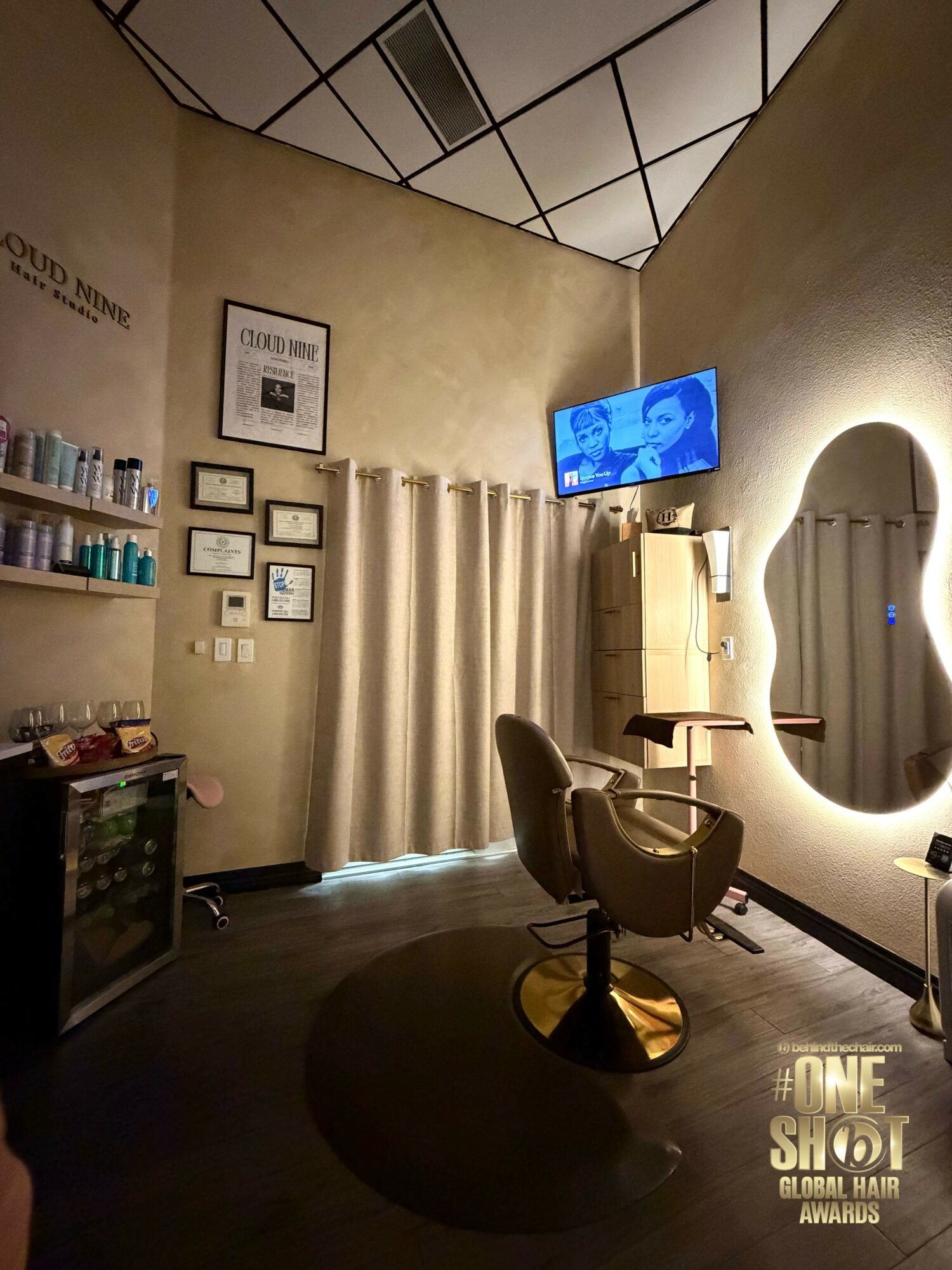 Salon interior with a chair, mirror, TV, and shelves with products, illuminated by warm lighting.