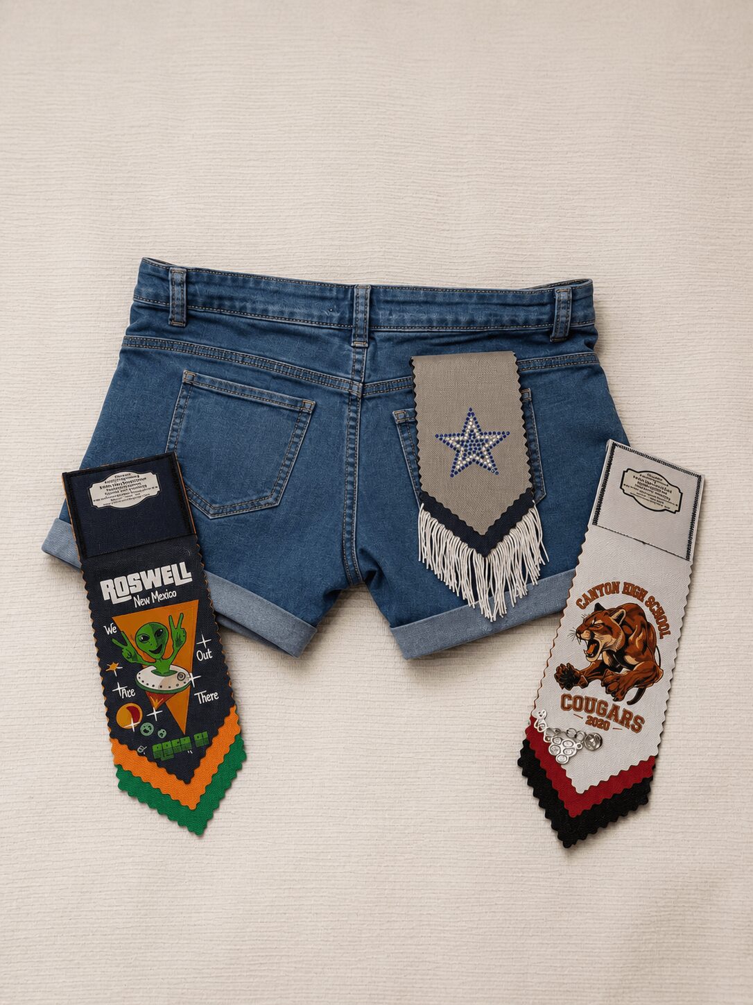 Pair of denim shorts with three colorful patches attached, displayed against a plain background.