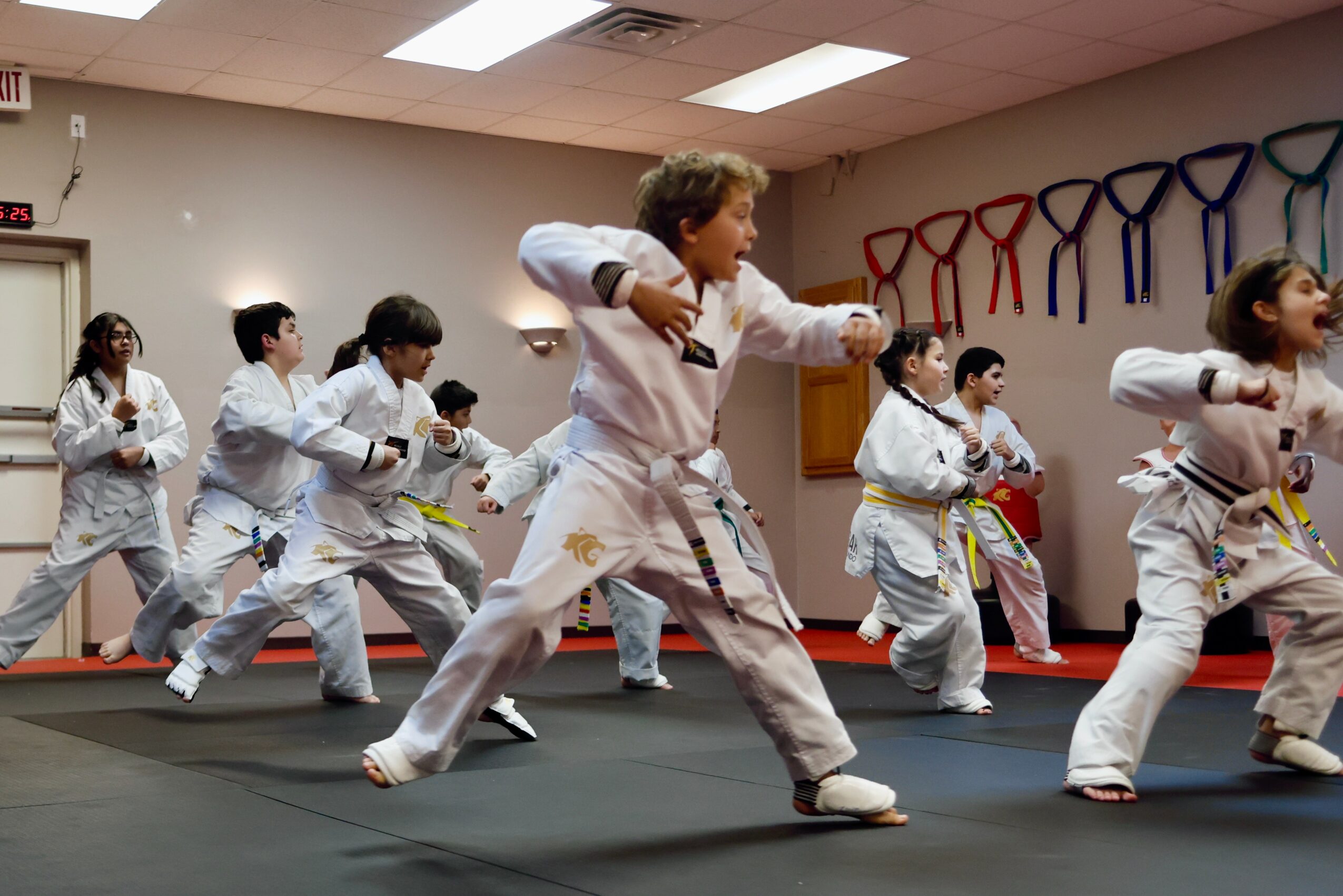 Group of children practicing martial arts in a dojo, wearing white uniforms, with colored belts, performing a synchronized move.