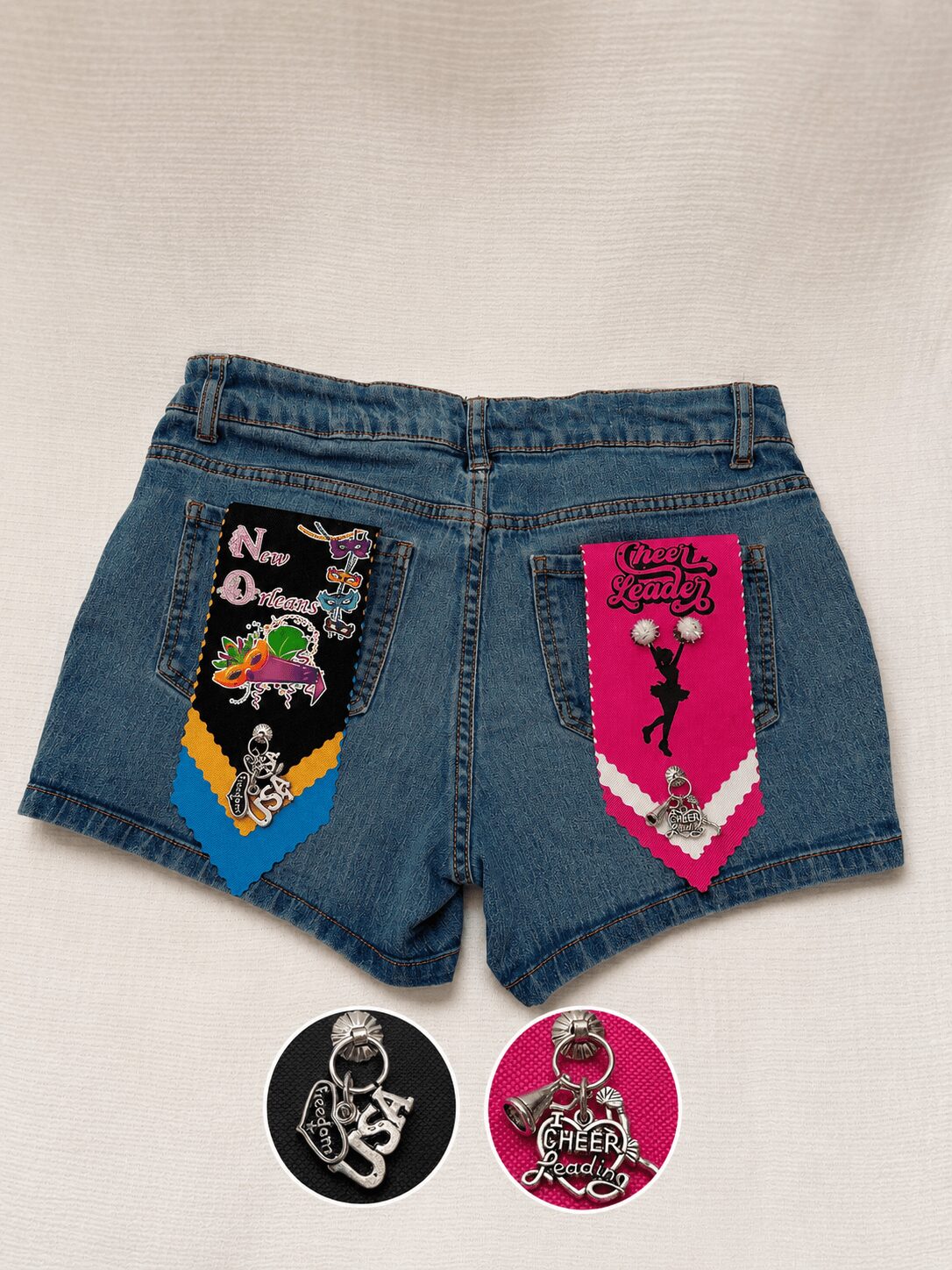 Denim shorts with colorful patches, including a unicorn and a girl with a bow, on a plain background.