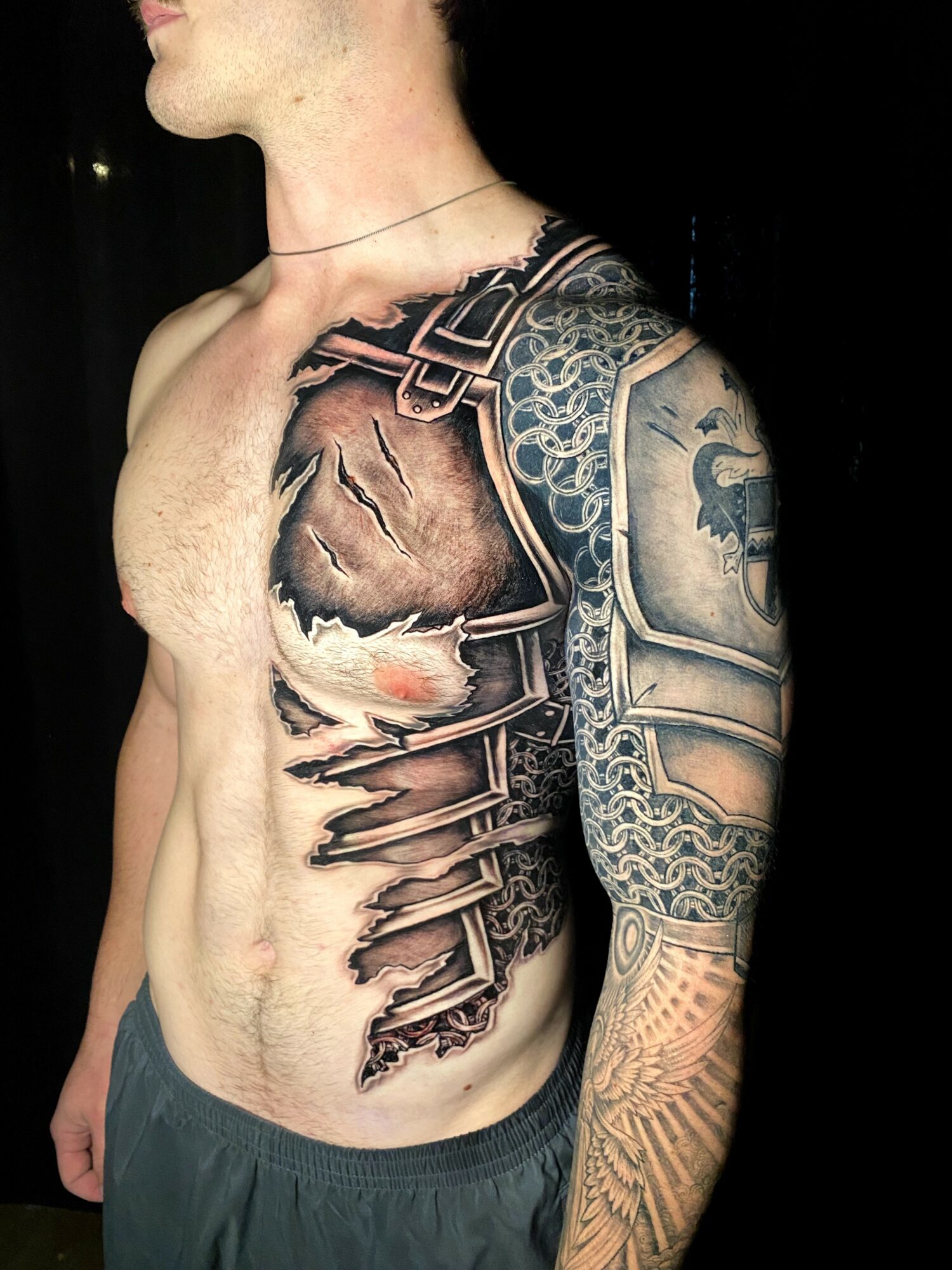 Side view of a person with a large chest and arm tattoo featuring a detailed, realistic design with various patterns.