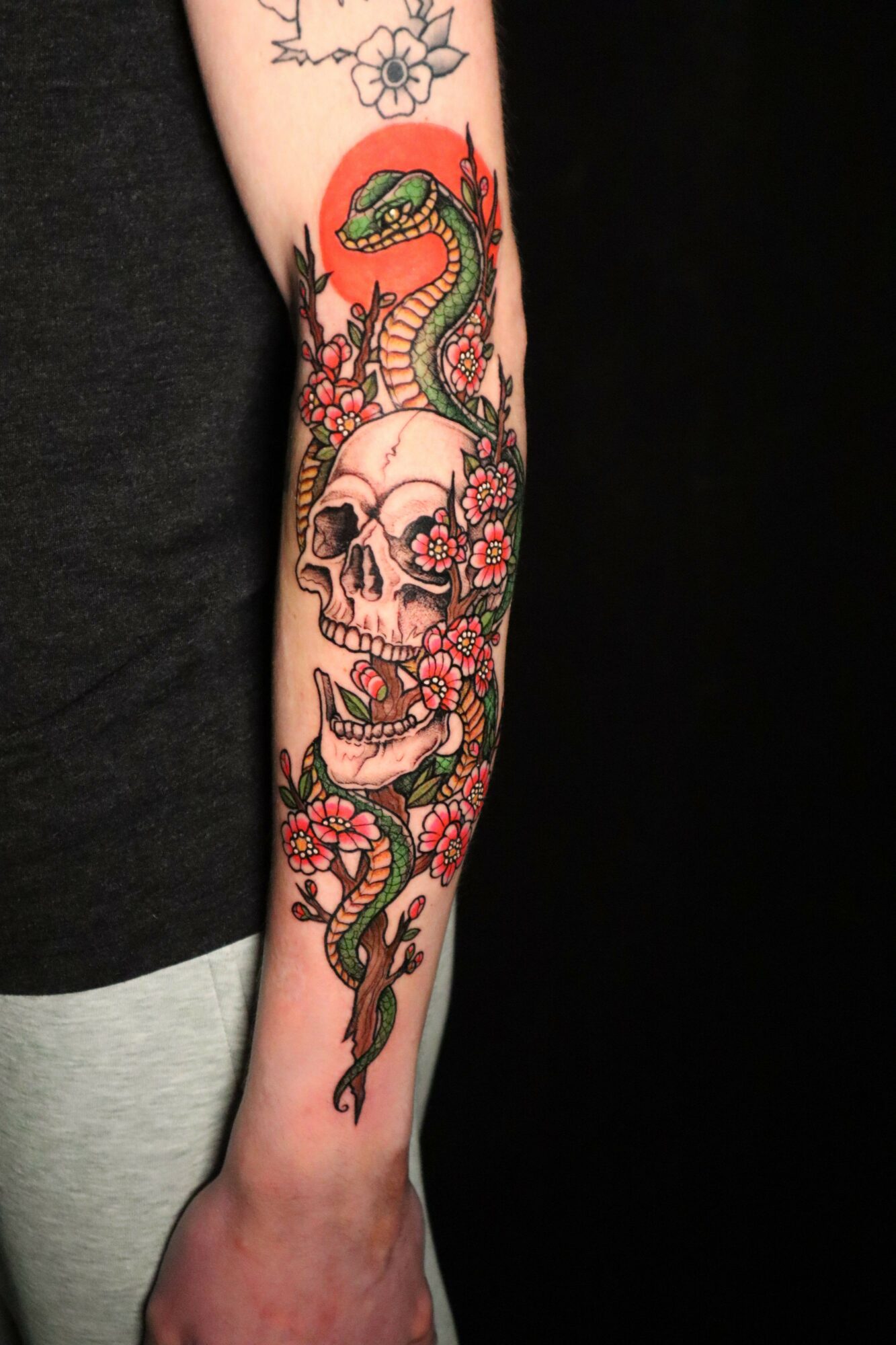 Tattoo of a snake coiled around a skull with flowers on the arm, colorful and detailed.