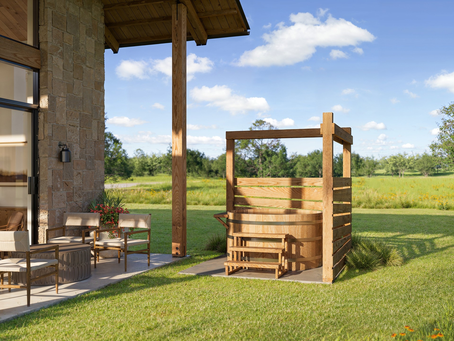 Wooden hot tub with a cover, outdoor setting with chairs, grass, trees, and blue sky with clouds