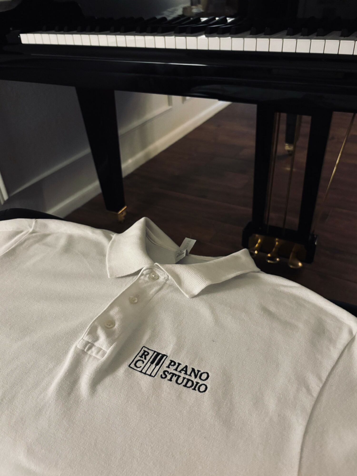 White shirt with 'Piano Studio' logo draped over a surface, with a piano in the background.