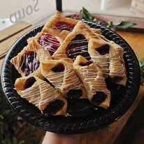 Pastry with chocolate and fruit on a black plate, on a wooden table, with a green leaf in the background.