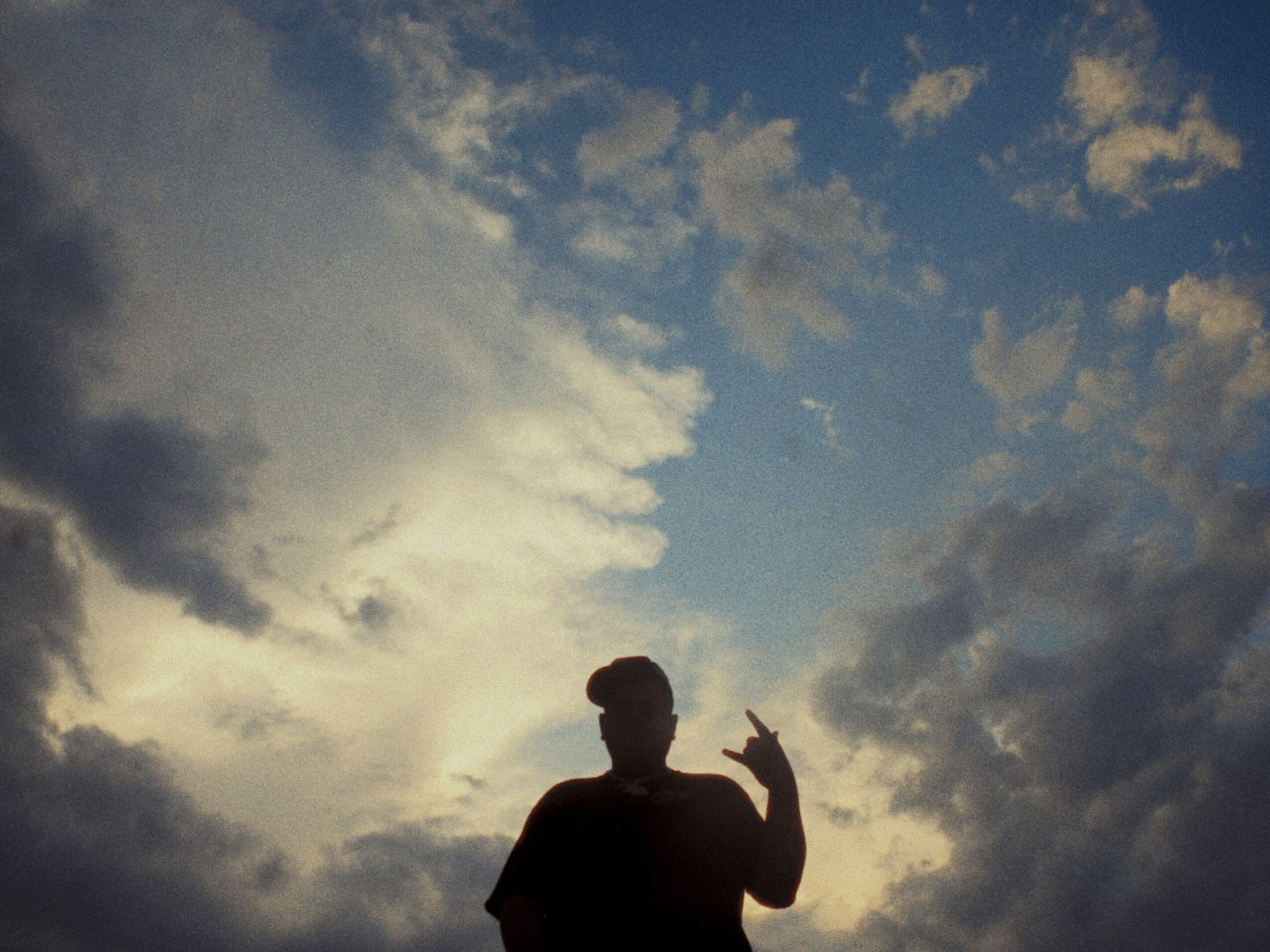 Silhouette of a person making a peace sign against a cloudy sky with sunlight breaking through.